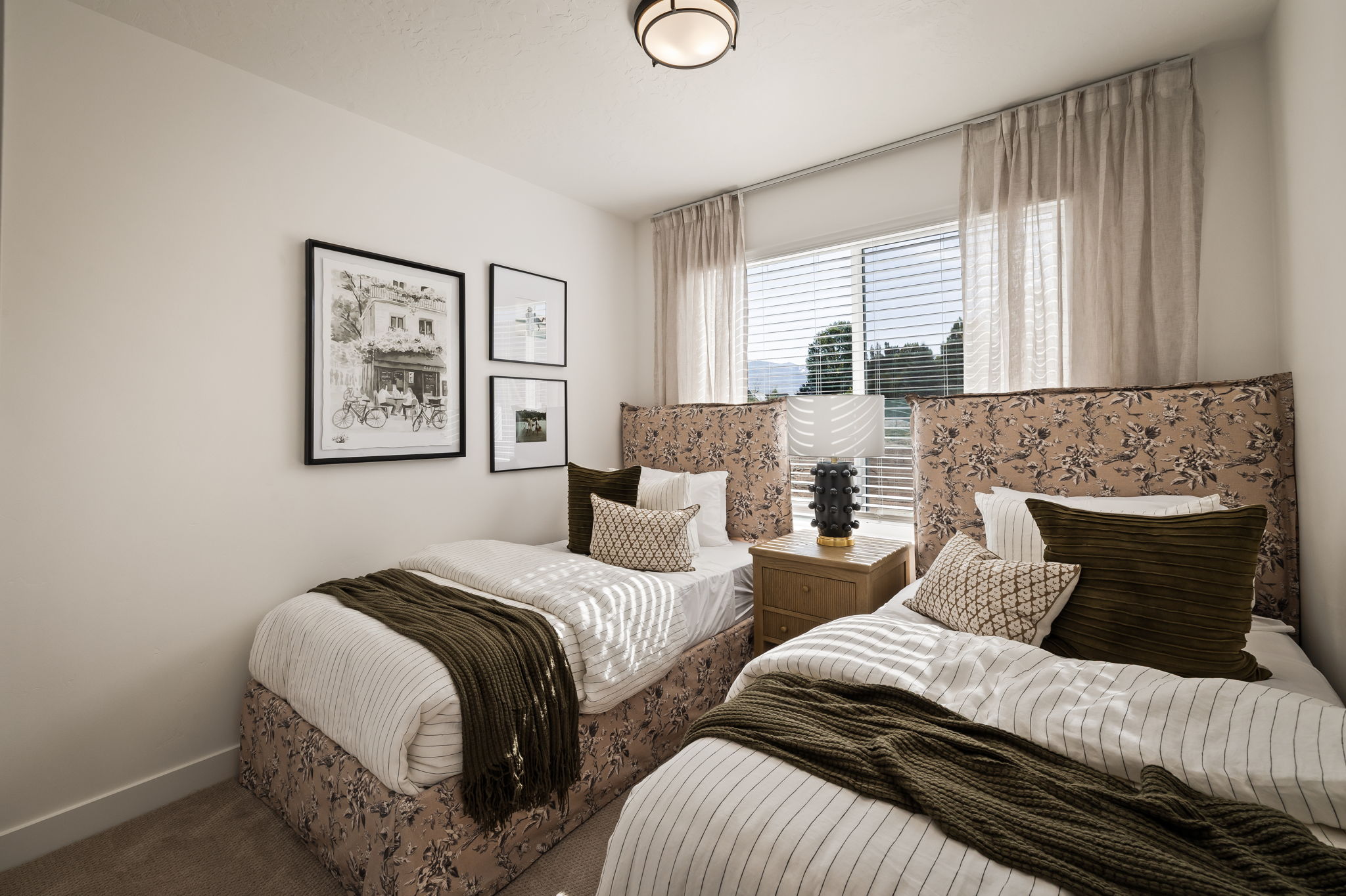 Bedroom featuring a large window with blinds and sheer drapes, framed artwork, and a built-in ceiling light fixture
