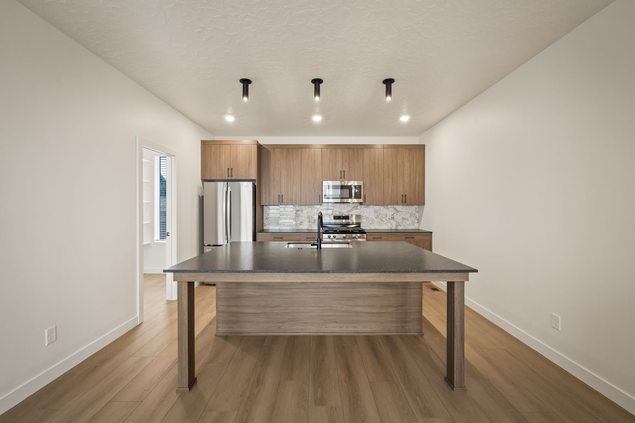 Kitchen featuring a large central island with dark countertop, wood-finish cabinetry, stainless steel appliances, and a tiled backsplash