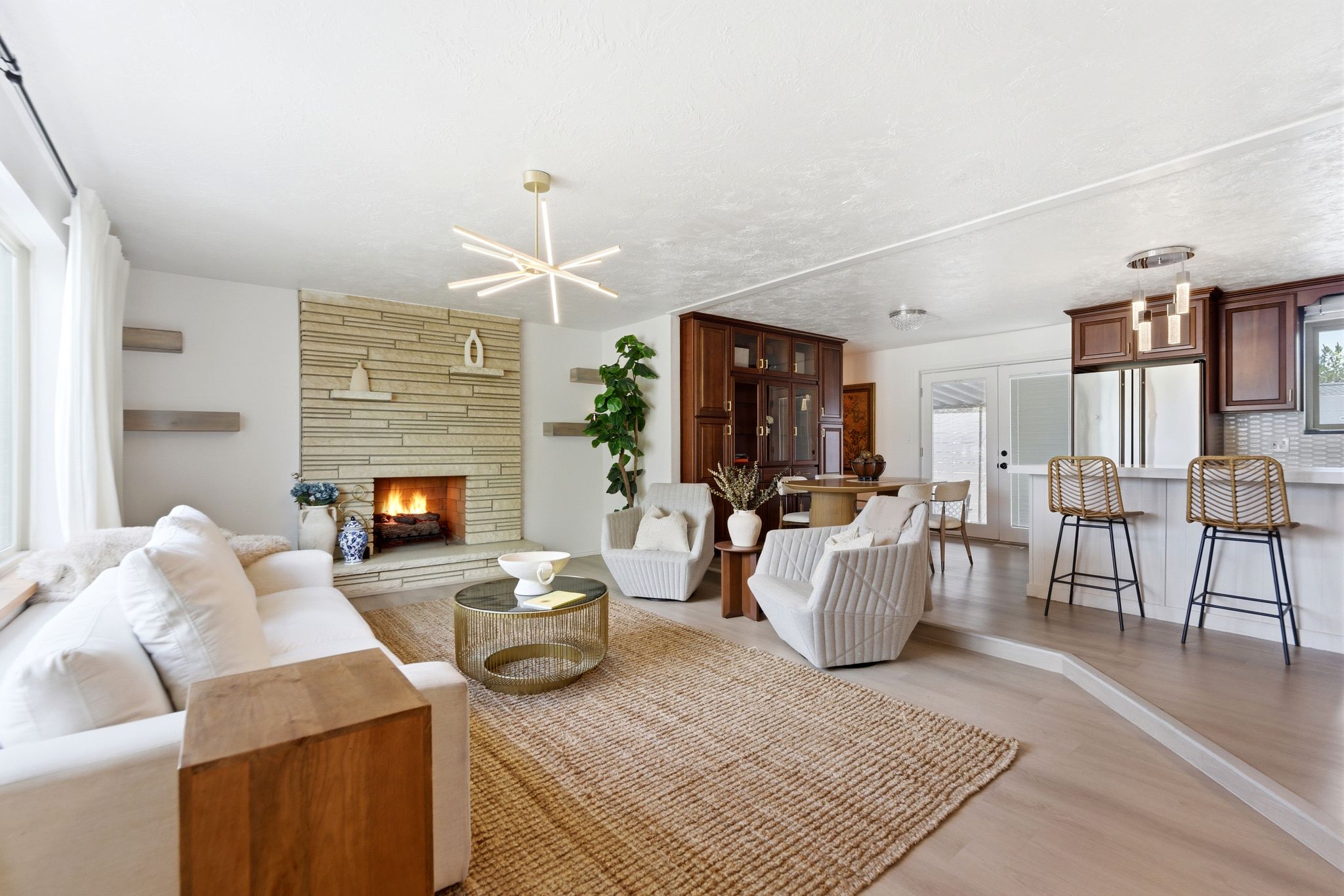 Open-concept living space featuring a stacked stone fireplace, light wood-finish flooring, and a contemporary linear chandelier