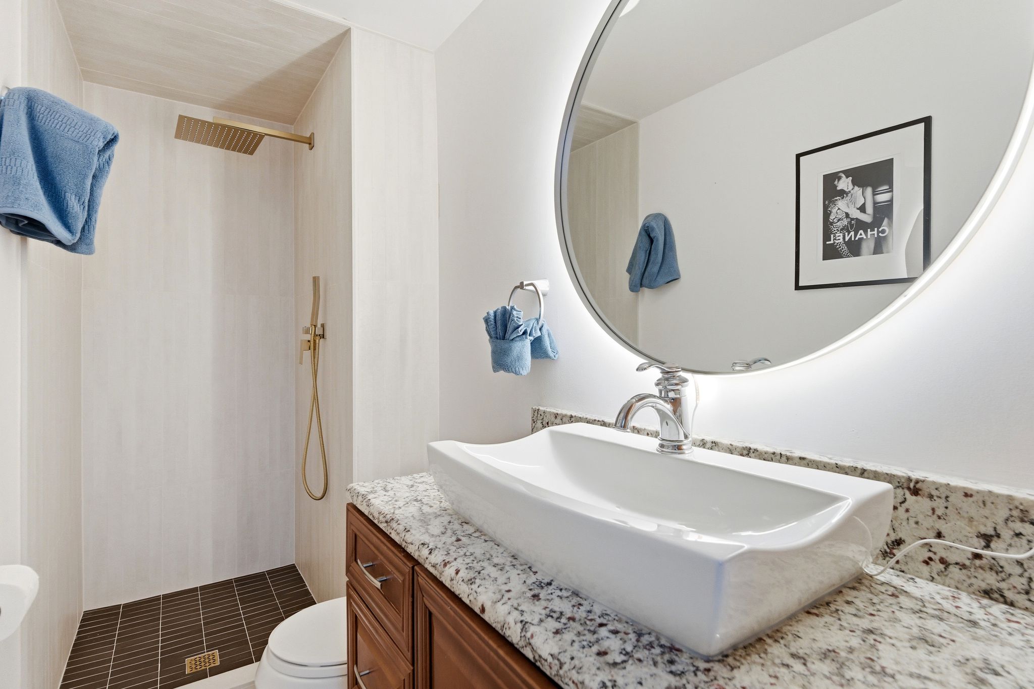 Modern bathroom featuring a vessel sink with a chrome faucet, granite-style countertop, and a lighted circular mirror