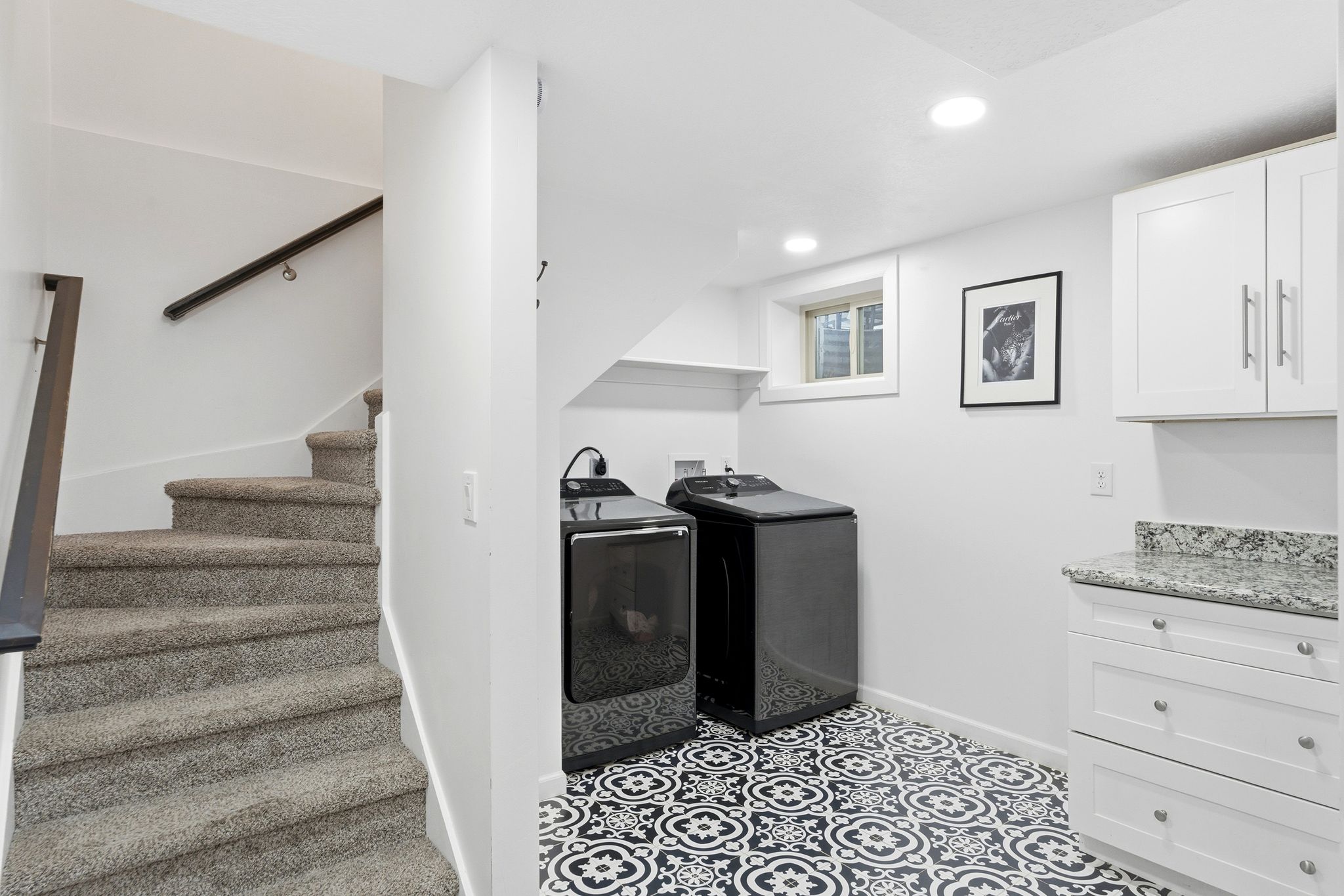 Laundry area featuring patterned floor tiles, white cabinetry with silver hardware, and a speckled countertop