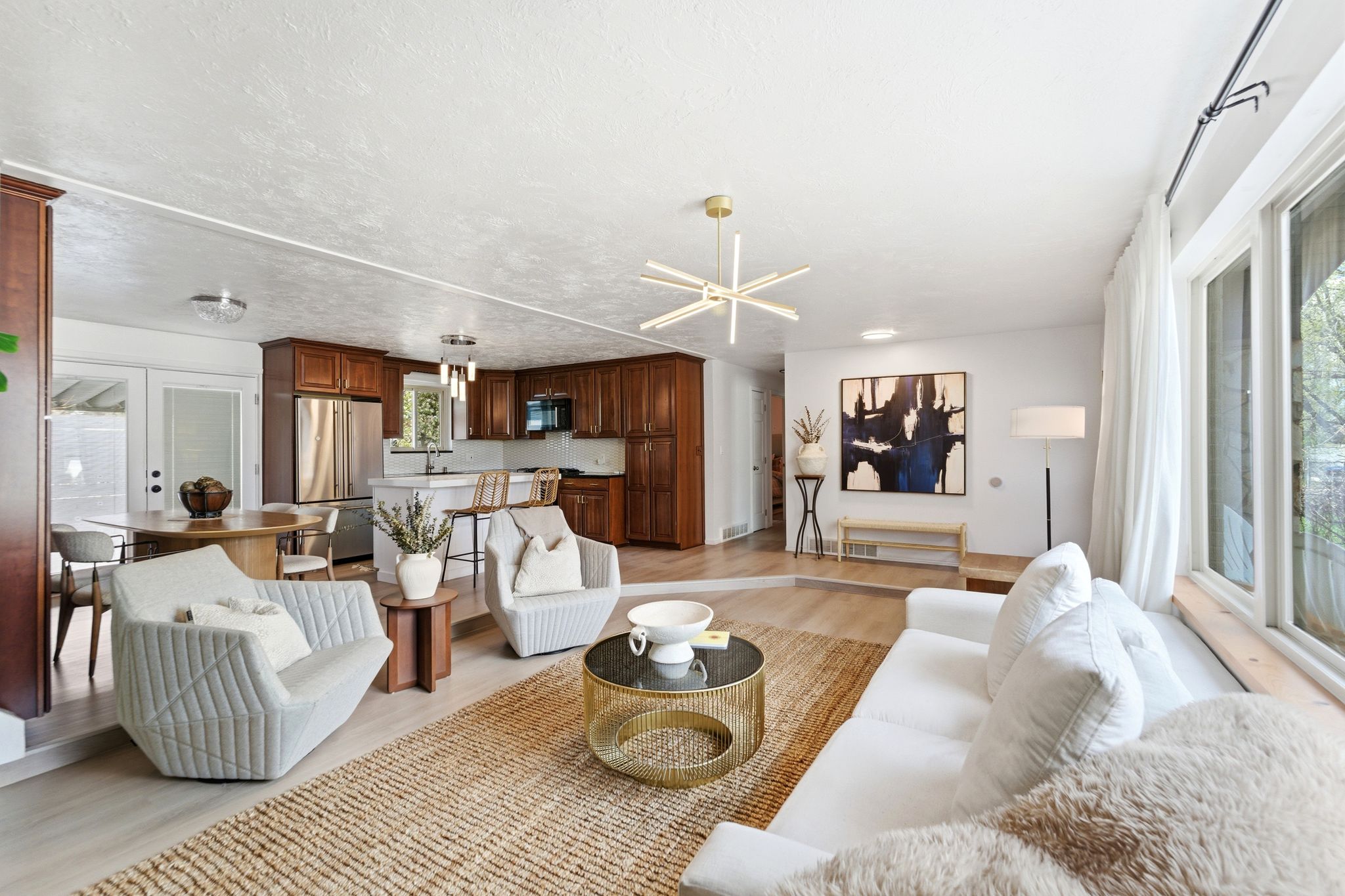 Open-concept living space featuring wood-finish flooring, a modern linear chandelier, and a kitchen with stainless steel appliances and wood cabinetry