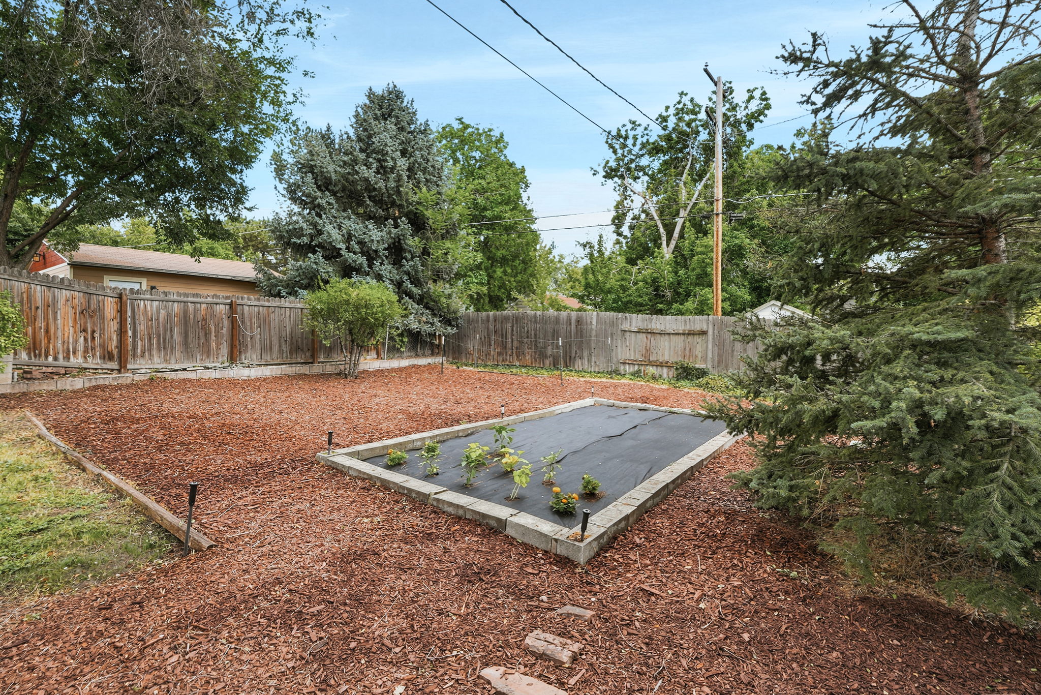 Expansive backyard featuring a raised garden bed, wood chip ground cover, and perimeter wood fencing