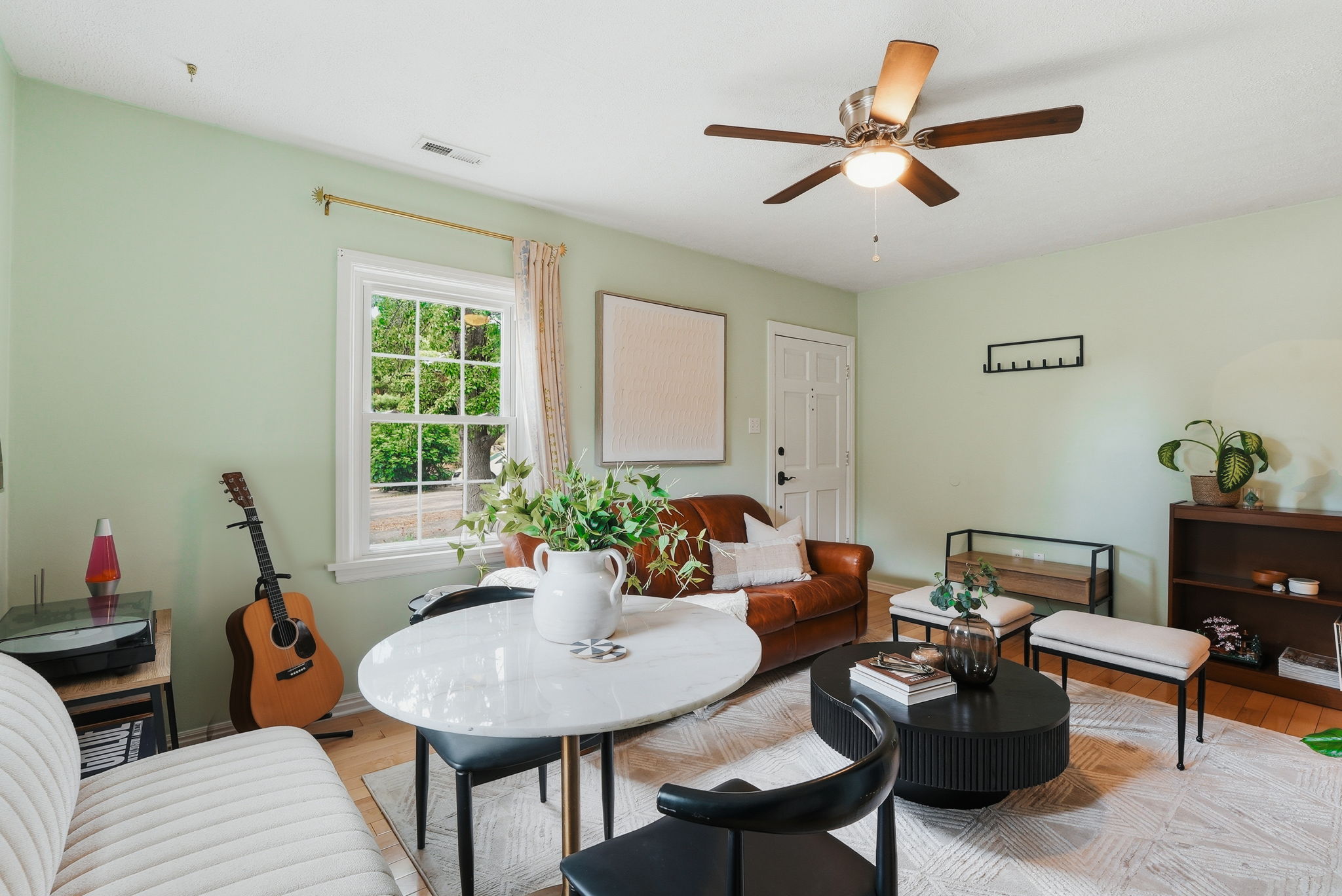 Living area featuring light wood-finish flooring, a multi-paned window, a ceiling fan with integrated lighting, and a paneled entry door