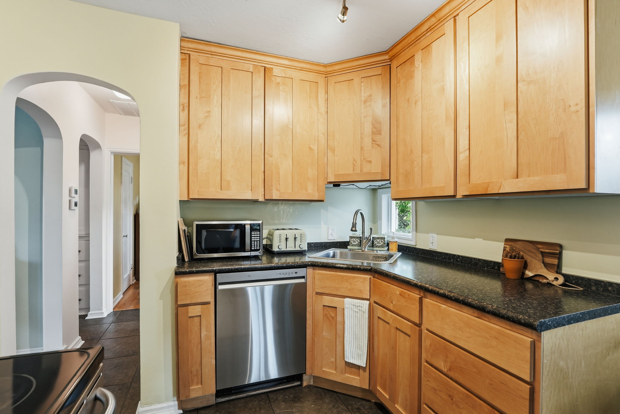 Kitchen with wood cabinetry, dark speckled countertops, stainless steel dishwasher, and an undermount sink with a gooseneck faucet