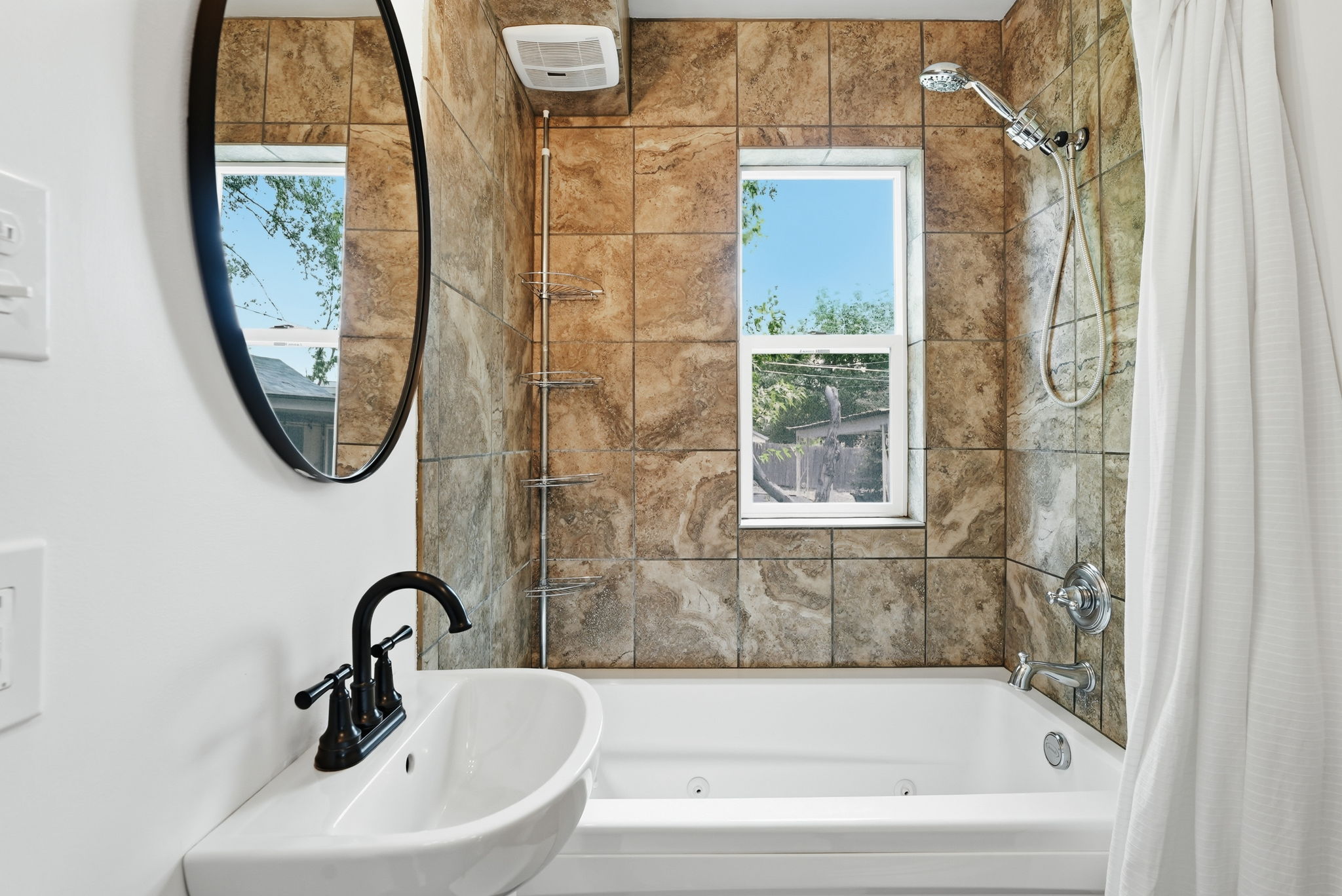 Bathroom featuring a jetted tub, ceramic wall tiles, a wall-mounted sink with matte black faucet, and an oval mirror