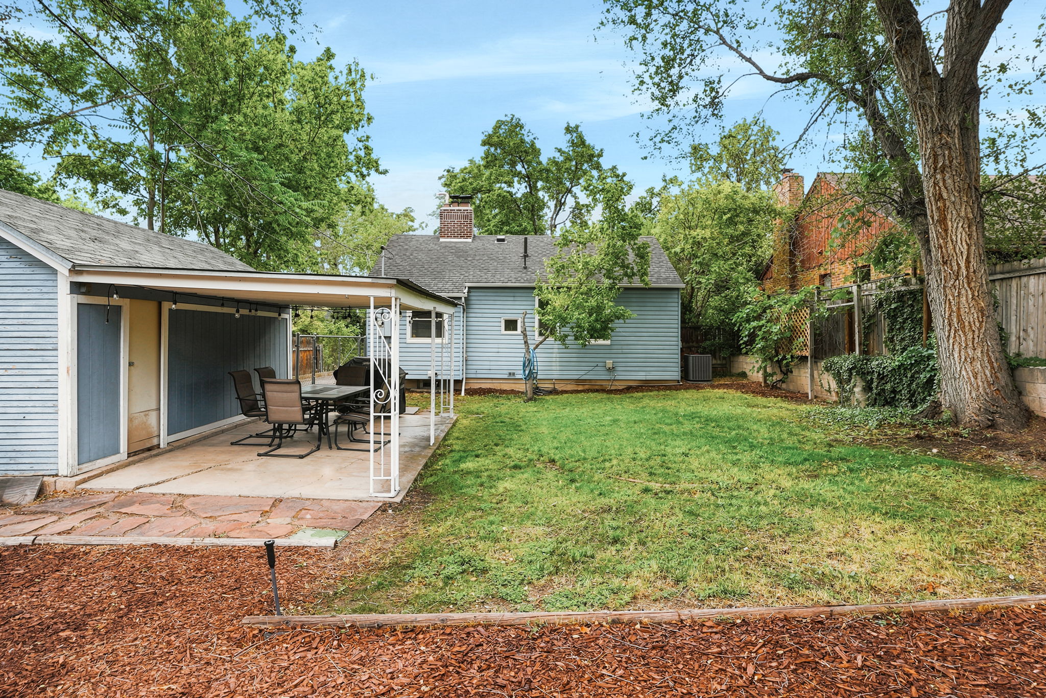 Expansive backyard featuring a covered patio with flagstone accents and a separate storage shed