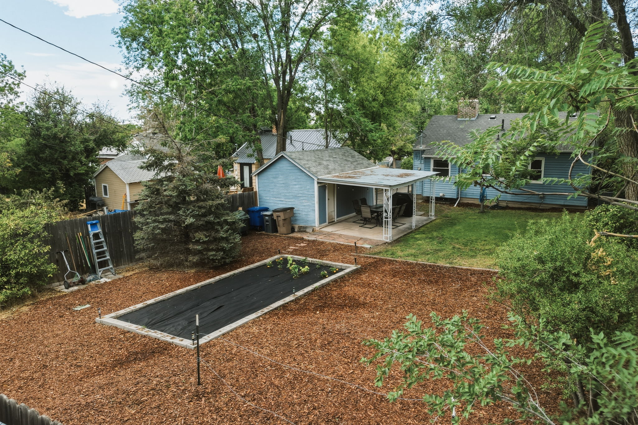 Expansive backyard featuring a covered patio, a detached structure with a metal roof, and a raised garden bed