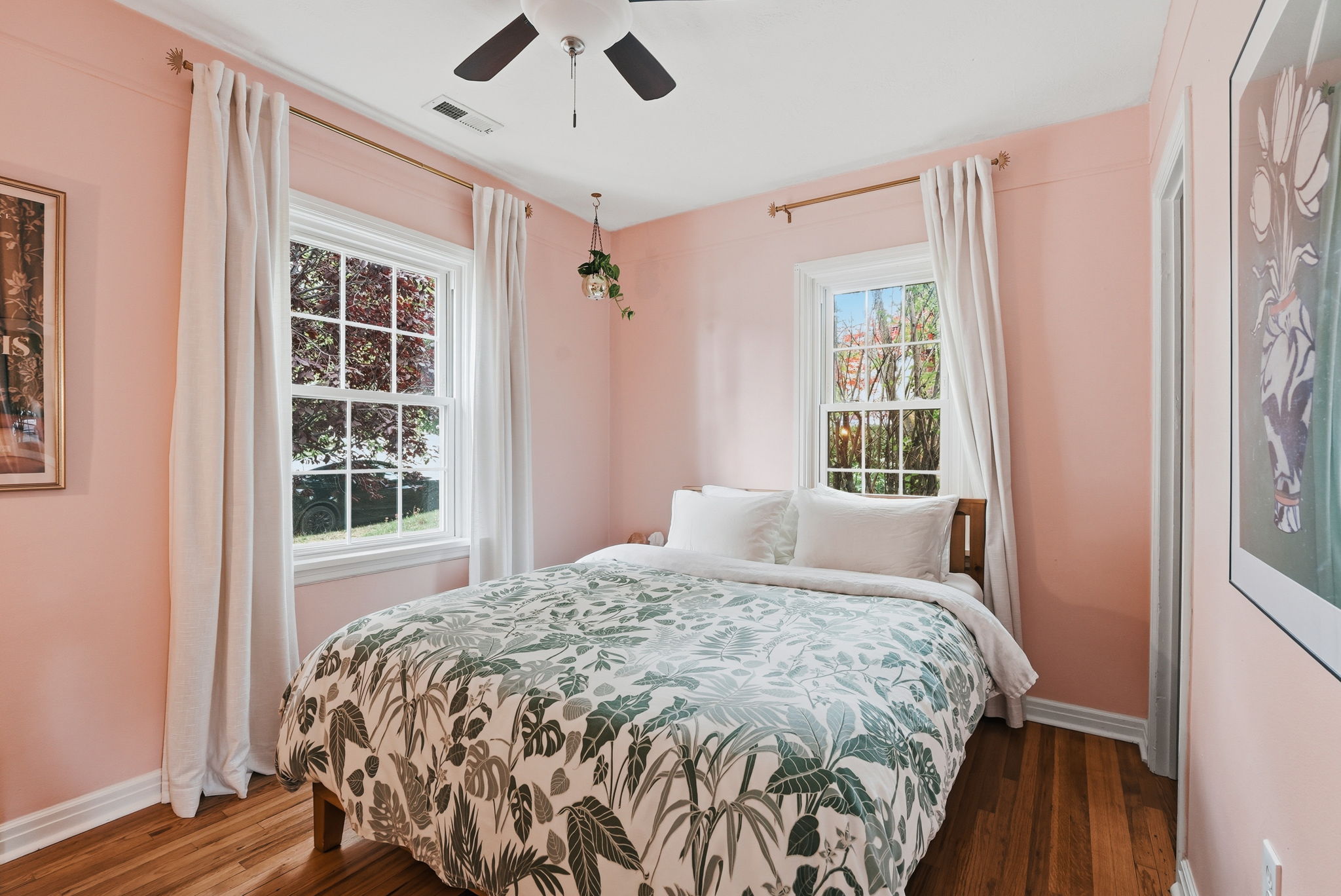 Bedroom featuring two double-hung windows with white trim, hardwood flooring, and a ceiling fan