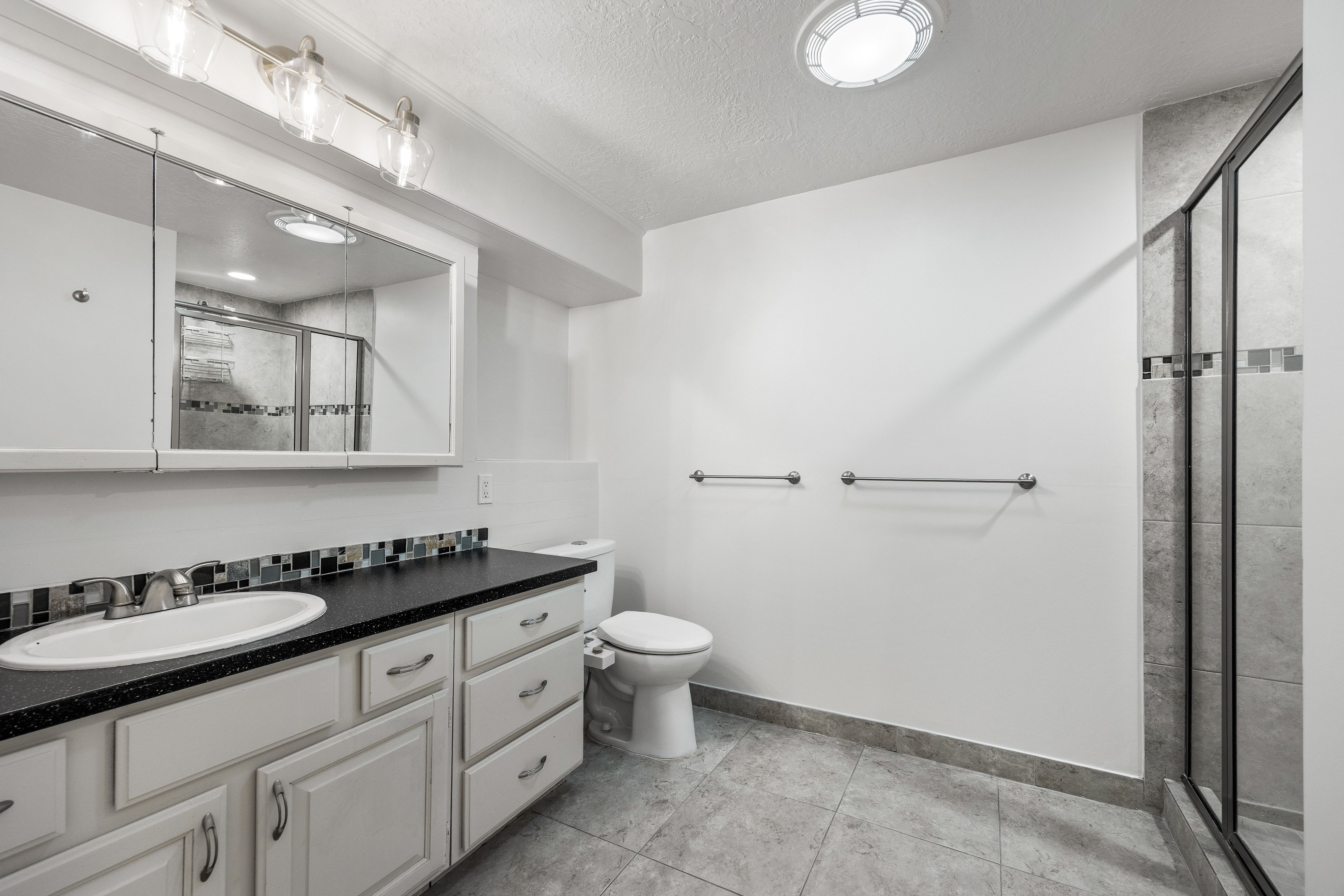 Bathroom featuring a white vanity with multiple drawers, a dark countertop, and an oval sink
