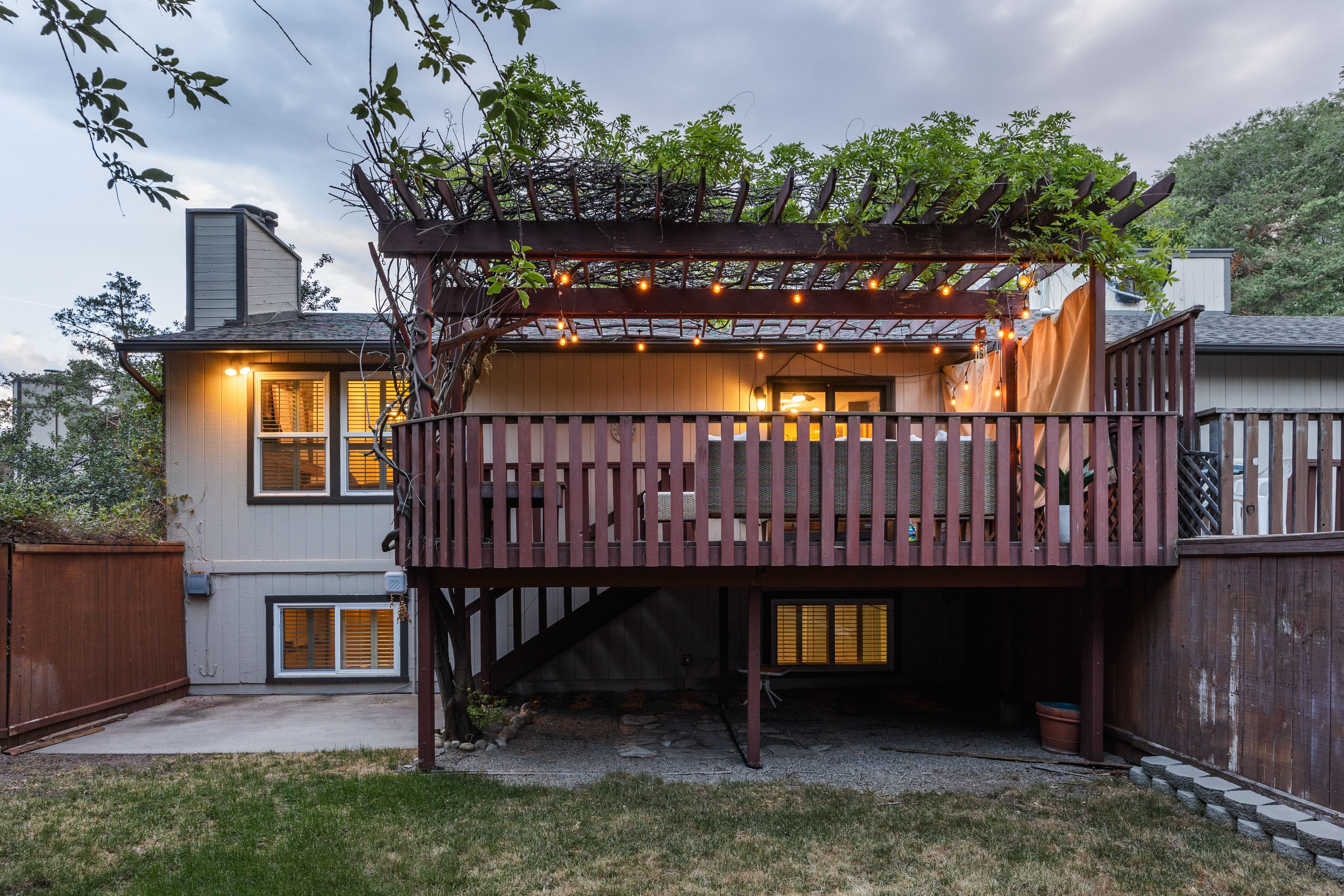 Multi-level deck featuring a pergola with string lights and established greenery