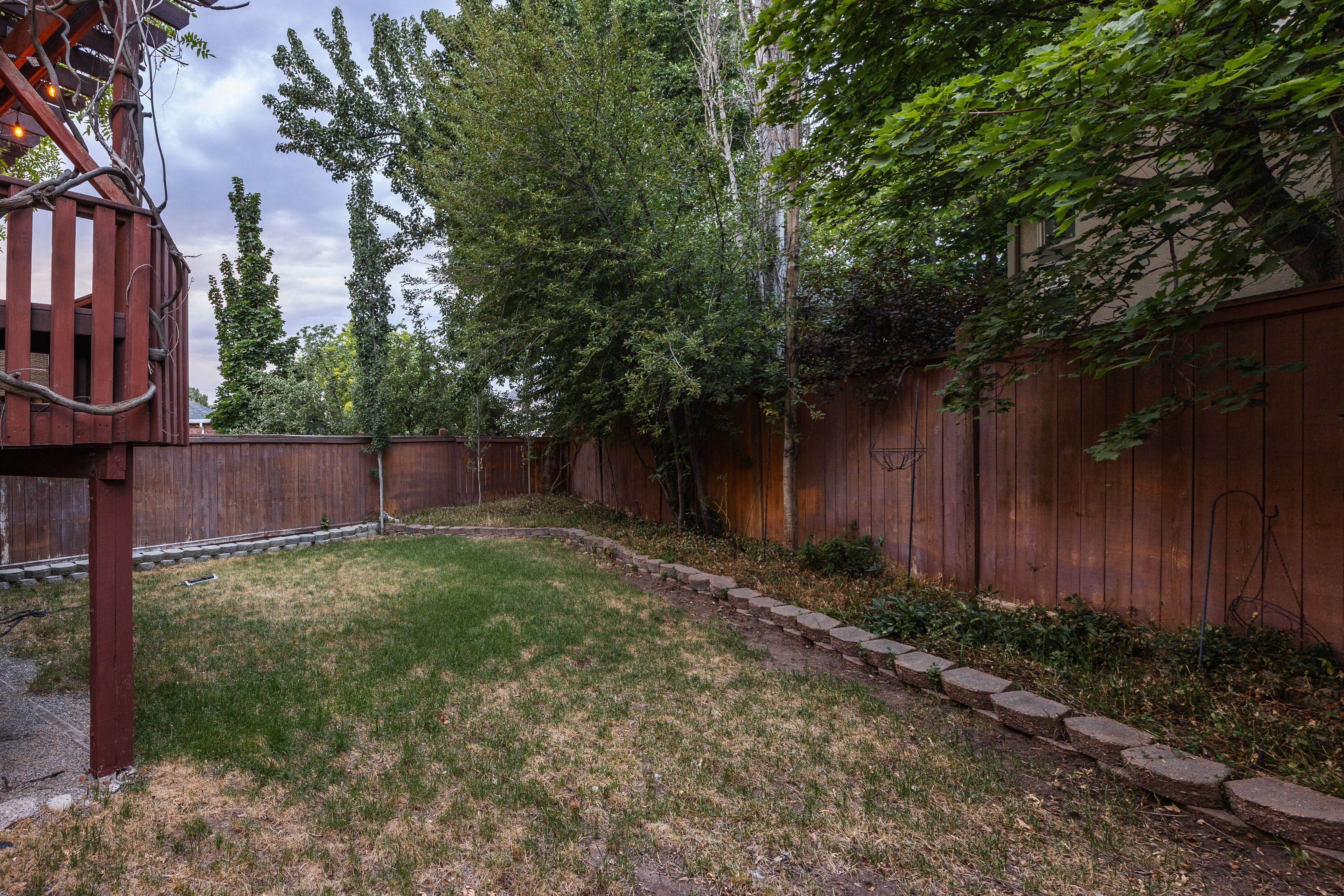 Expansive backyard featuring a manicured lawn, established trees, and a privacy fence