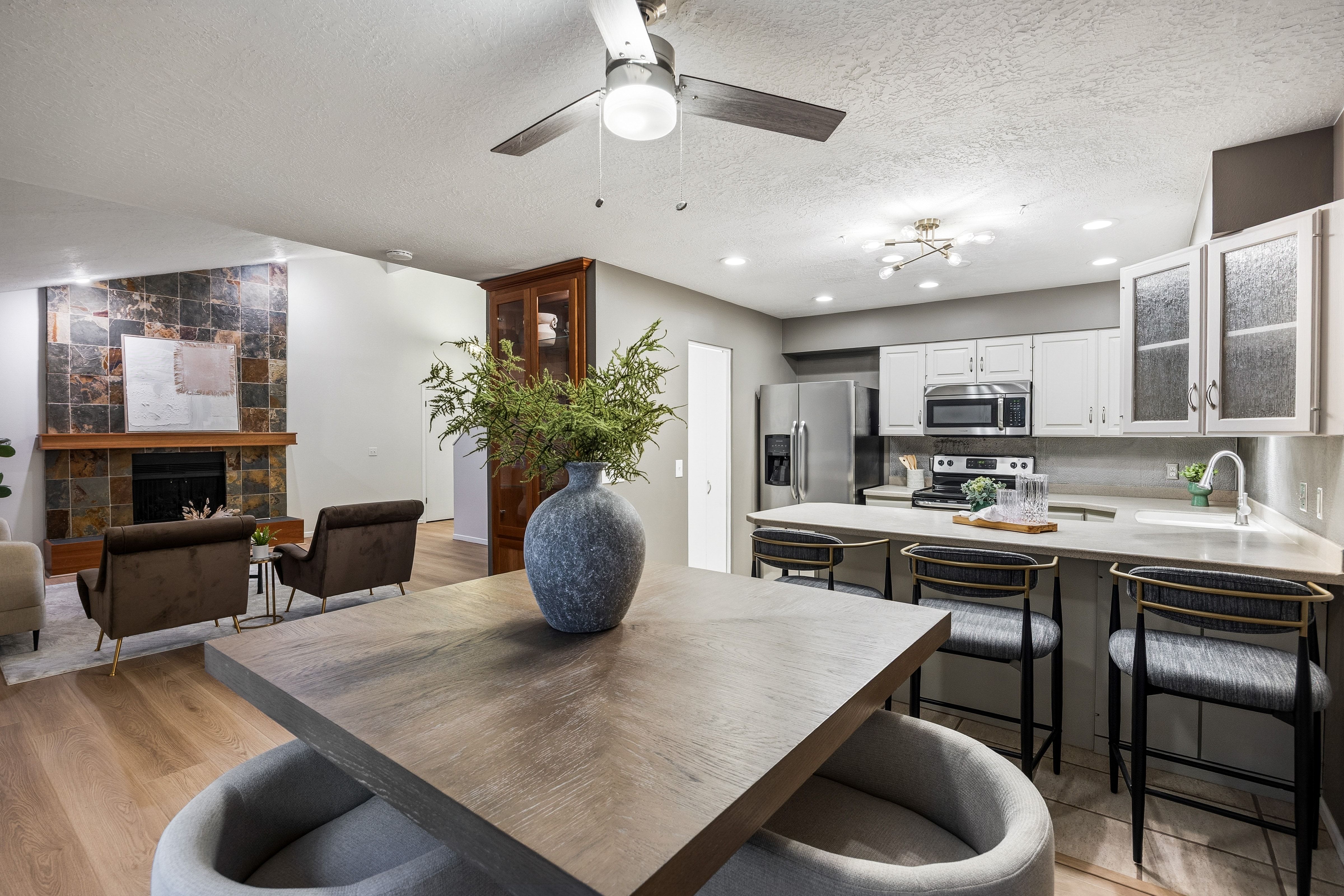 Open-concept living space featuring wood-finish flooring, a contemporary kitchen with stainless steel appliances, and a living area with a stone-accented fireplace