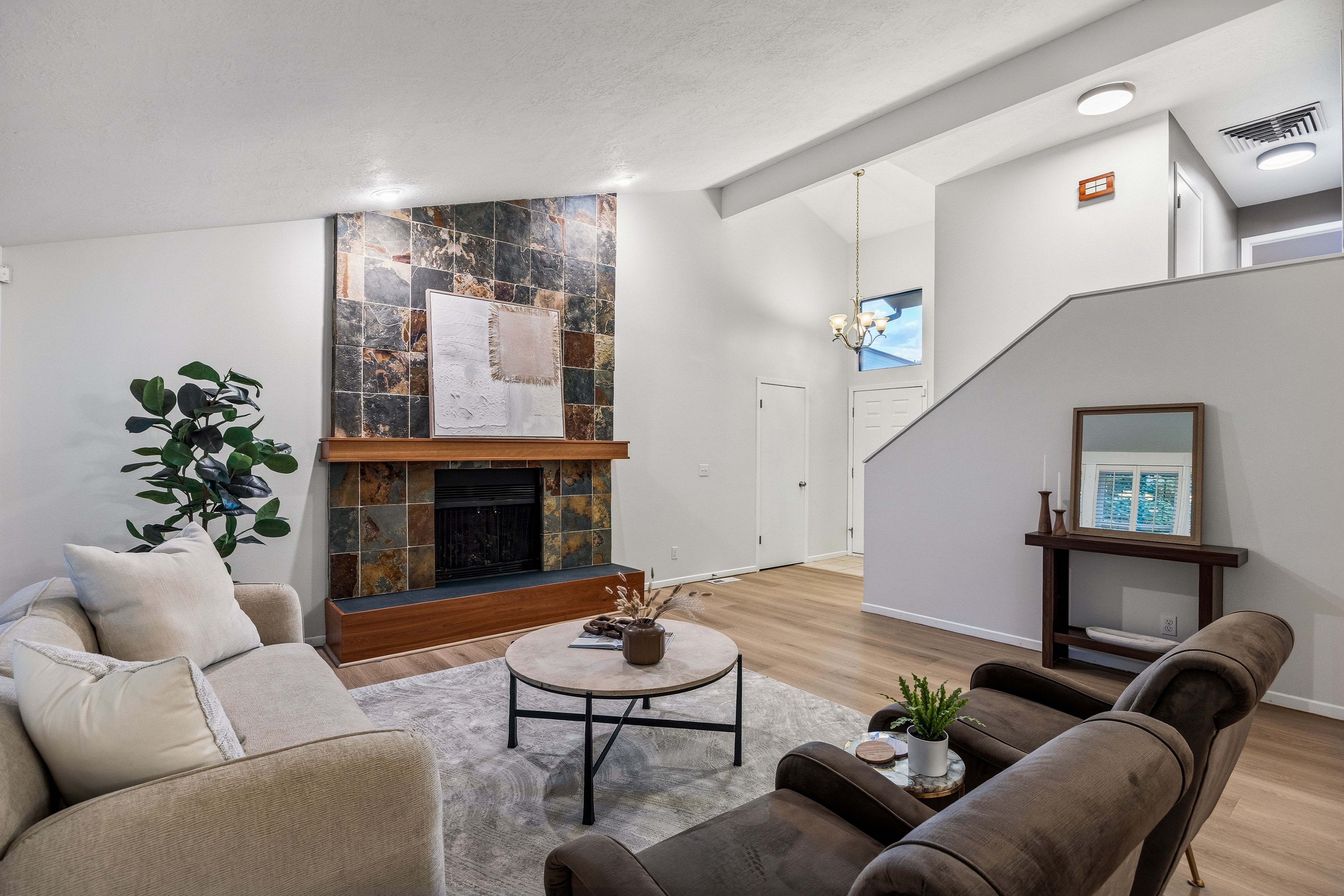 Living area featuring a floor-to-ceiling slate tile fireplace surround with a wood mantel, vaulted ceilings, wood-finish flooring, and a stairway with a partial wall