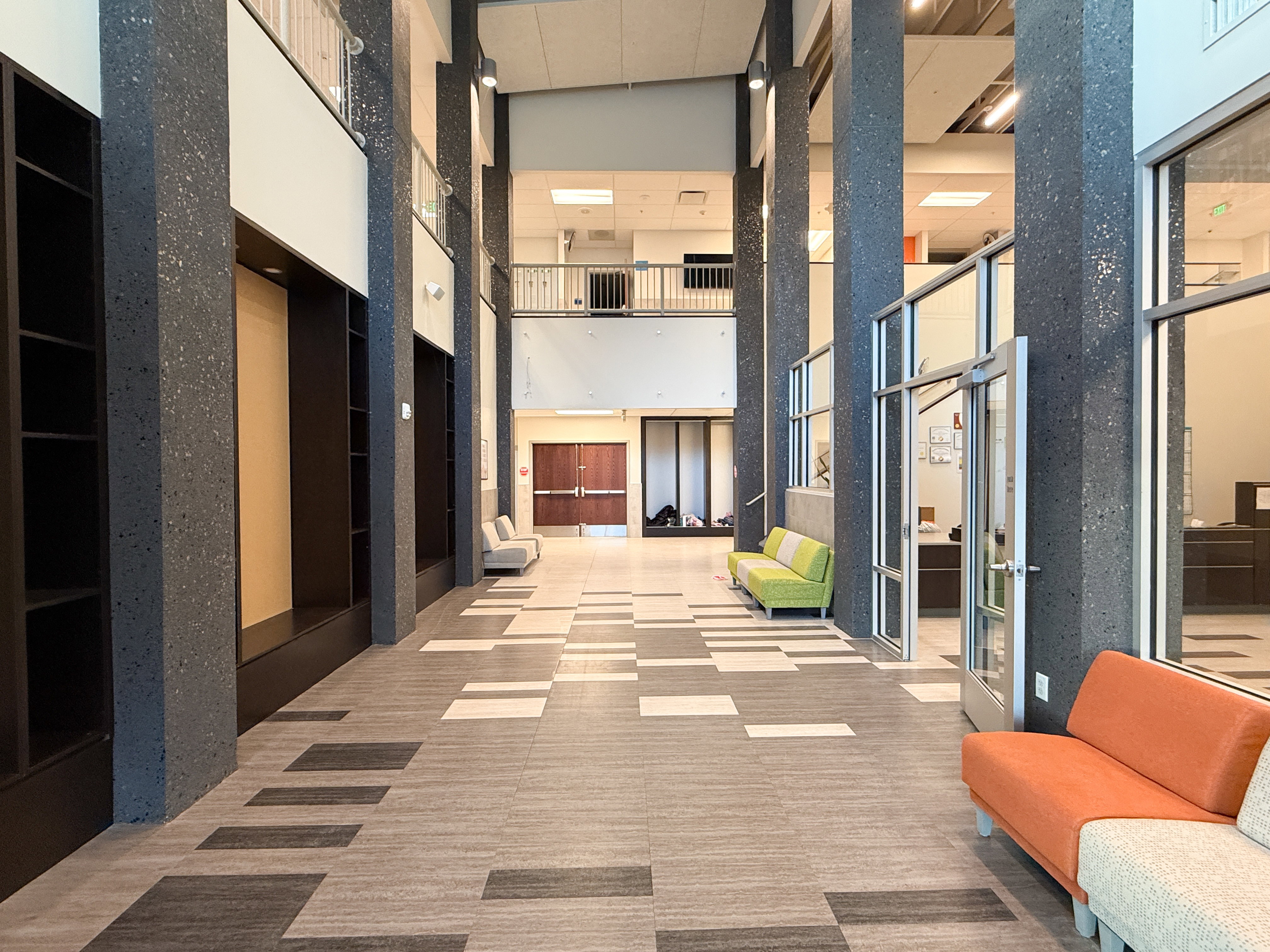 Spacious multi-story lobby featuring patterned tile flooring, exposed aggregate columns, and extensive built-in shelving