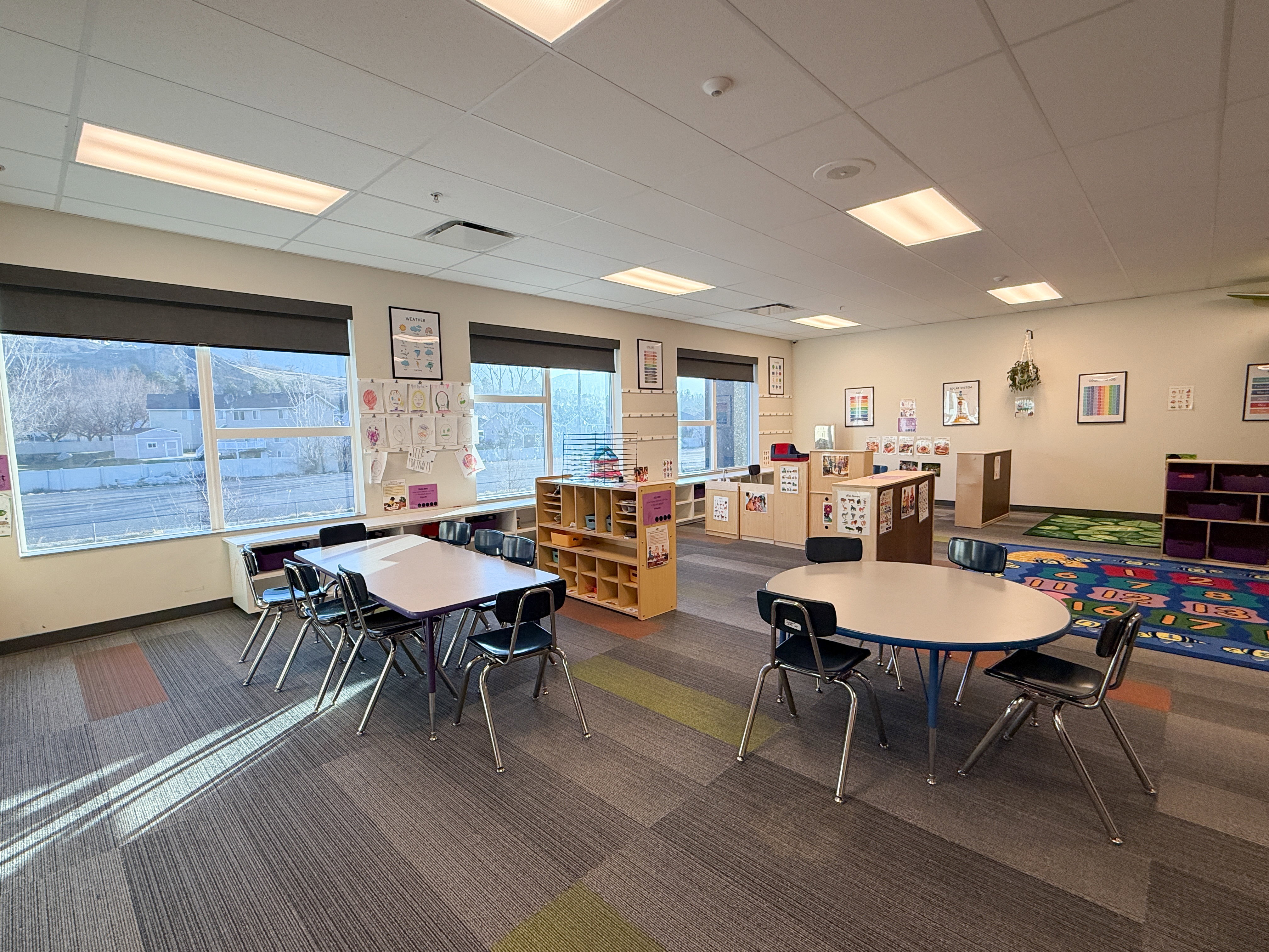 Spacious interior featuring large windows with dark roller shades, ceiling-mounted lighting, and modular carpet tile flooring