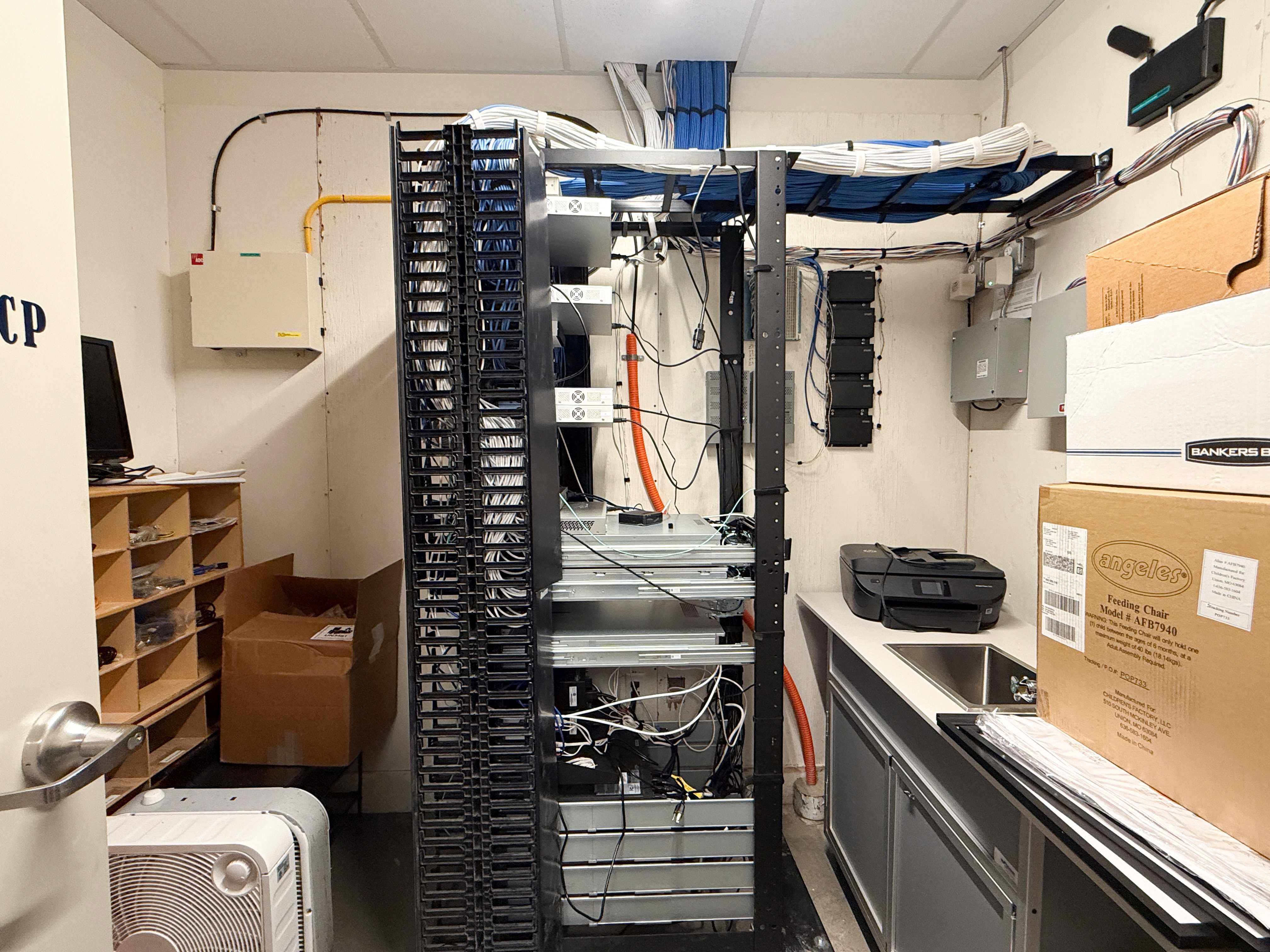 Dedicated utility room featuring extensive network infrastructure with structured cabling, a built-in countertop with an integrated sink, under-cabinet storage, and wood-finish shelving