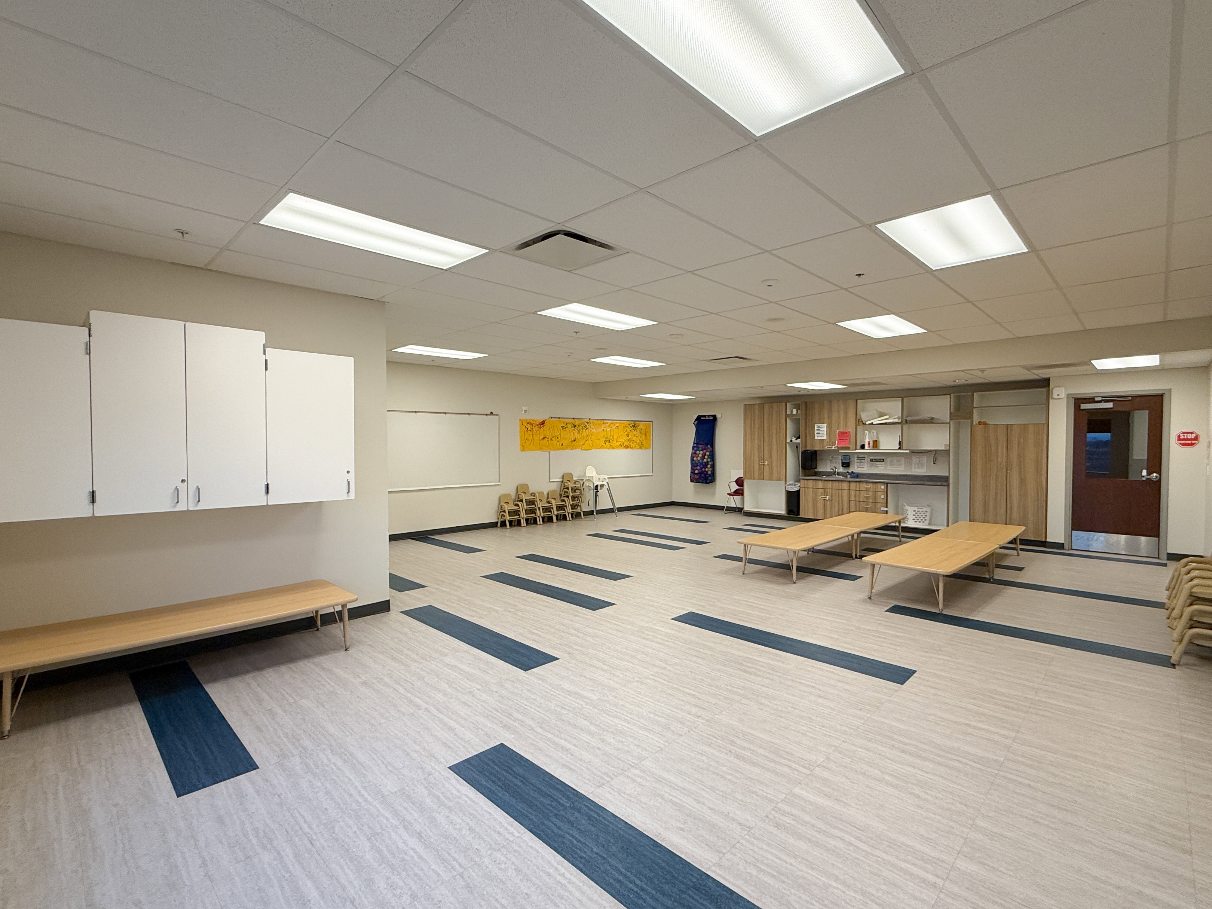 Spacious room featuring light-toned flooring with blue accents, recessed lighting, and a drop ceiling