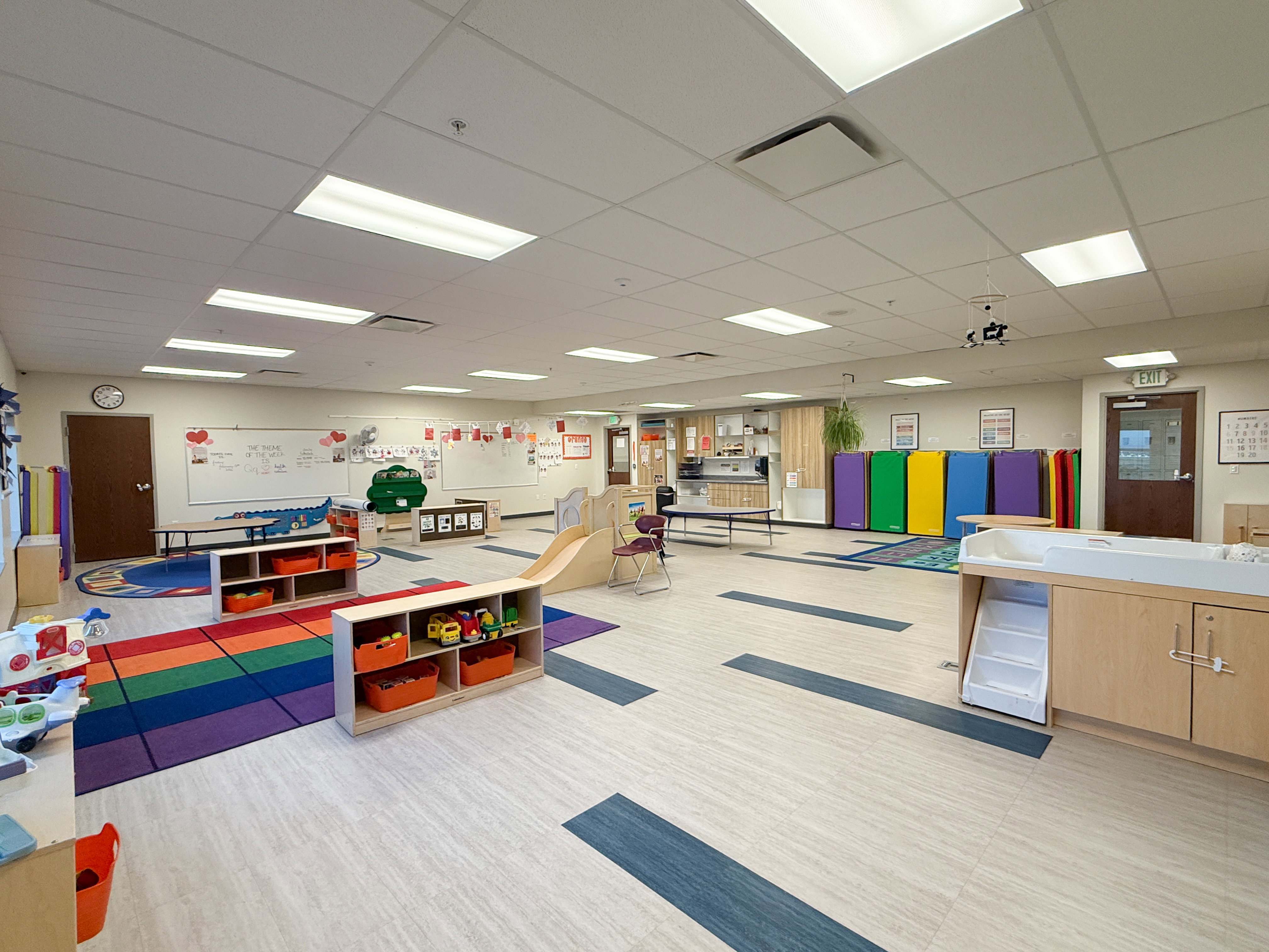 Spacious room featuring light-toned flooring with dark accent strips, drop ceiling with integrated lighting, and multiple wall-mounted whiteboards