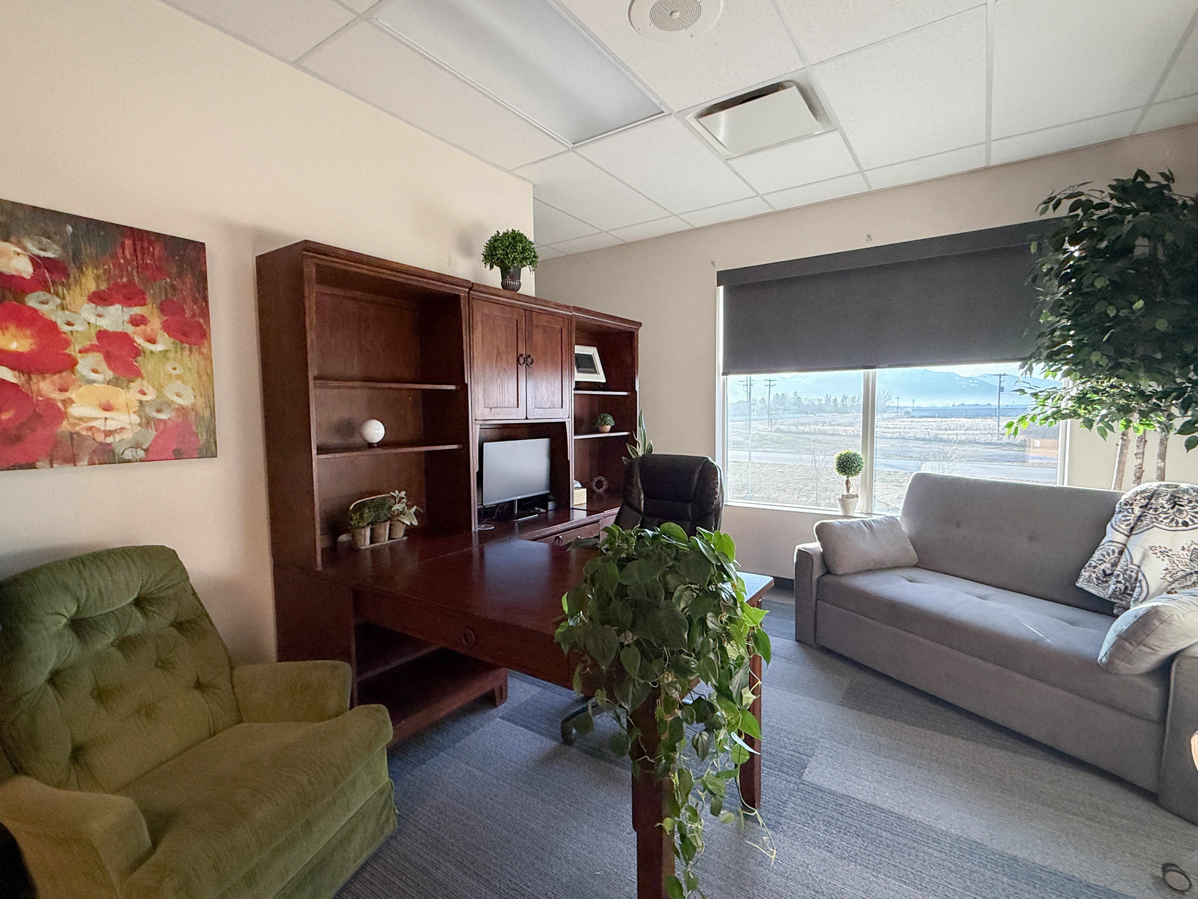 Office space featuring a large window, roller shade, and built-in wood-finish shelving and desk unit