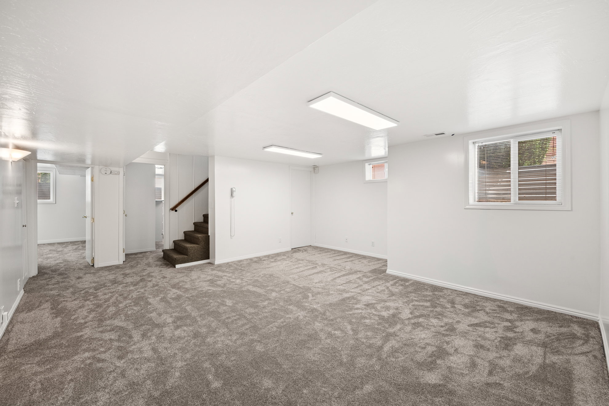 Spacious room featuring new gray carpeting, white walls, and bright overhead lighting