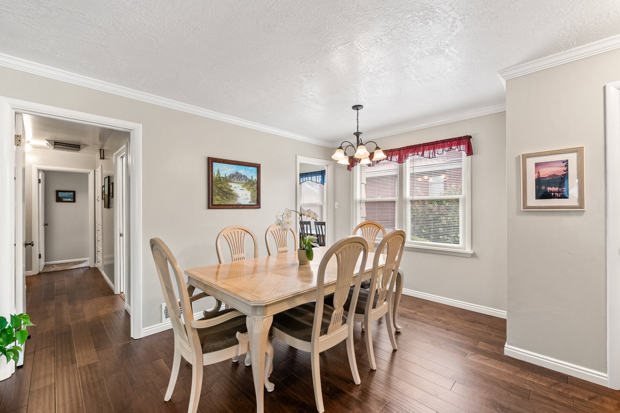 Dining area featuring dark wood-finish flooring, two windows with white trim, a multi-bulb chandelier, crown molding, and baseboards