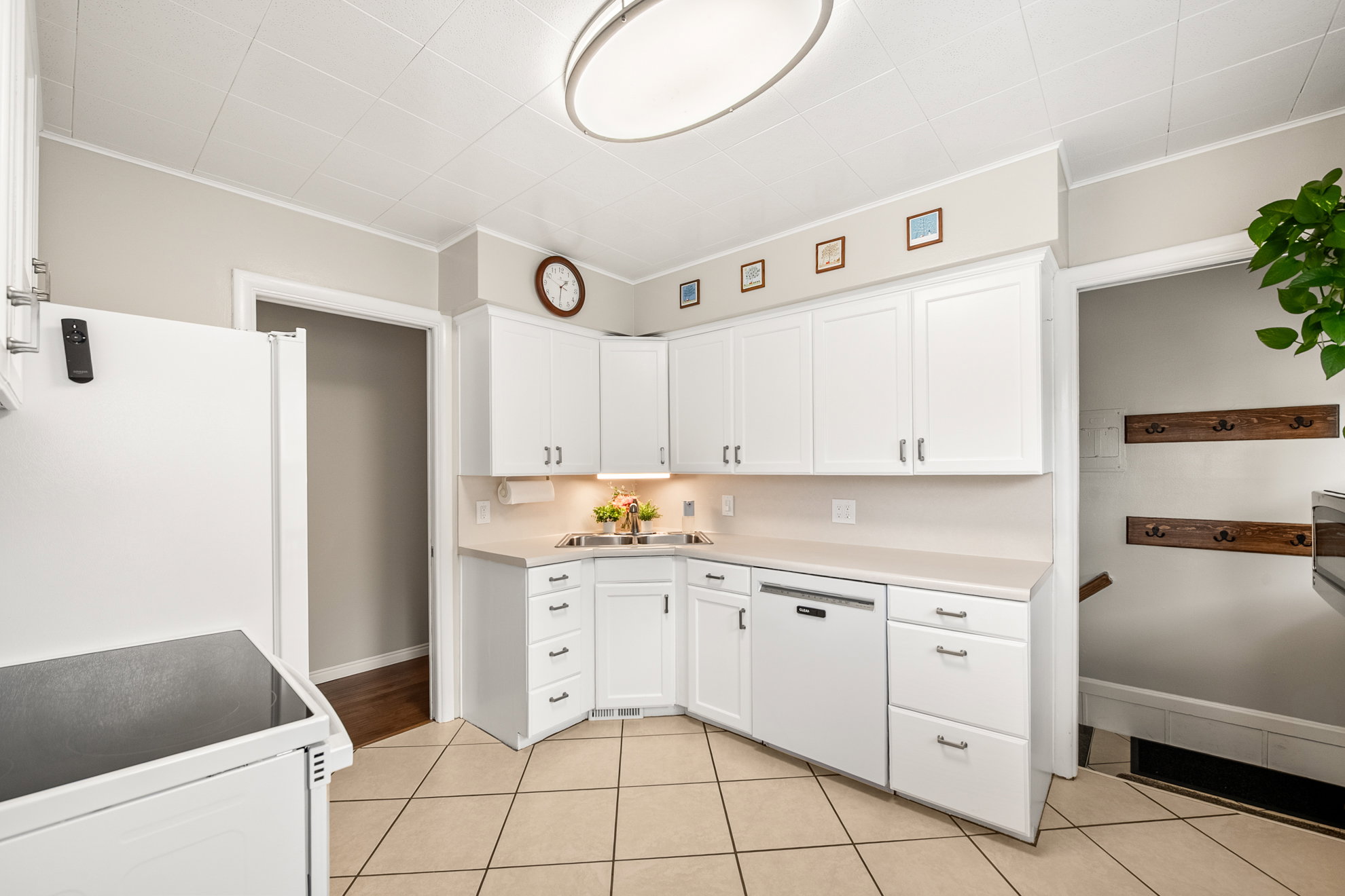 Bright kitchen featuring white cabinetry, light-toned countertops, a built-in dishwasher, and tile flooring