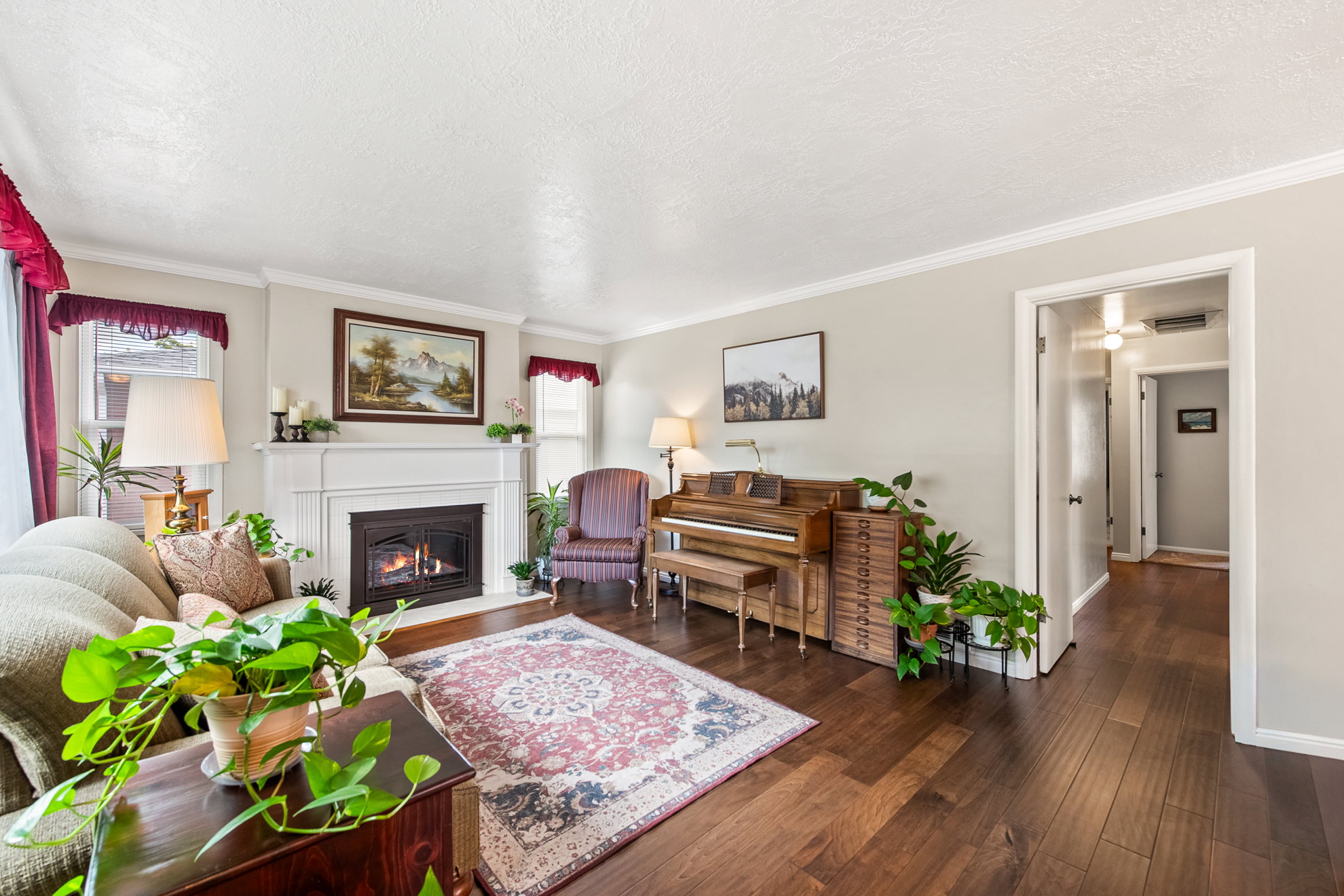 Living room featuring a prominent fireplace with a white mantel, rich wood-finish flooring, light neutral wall paint, and white crown molding