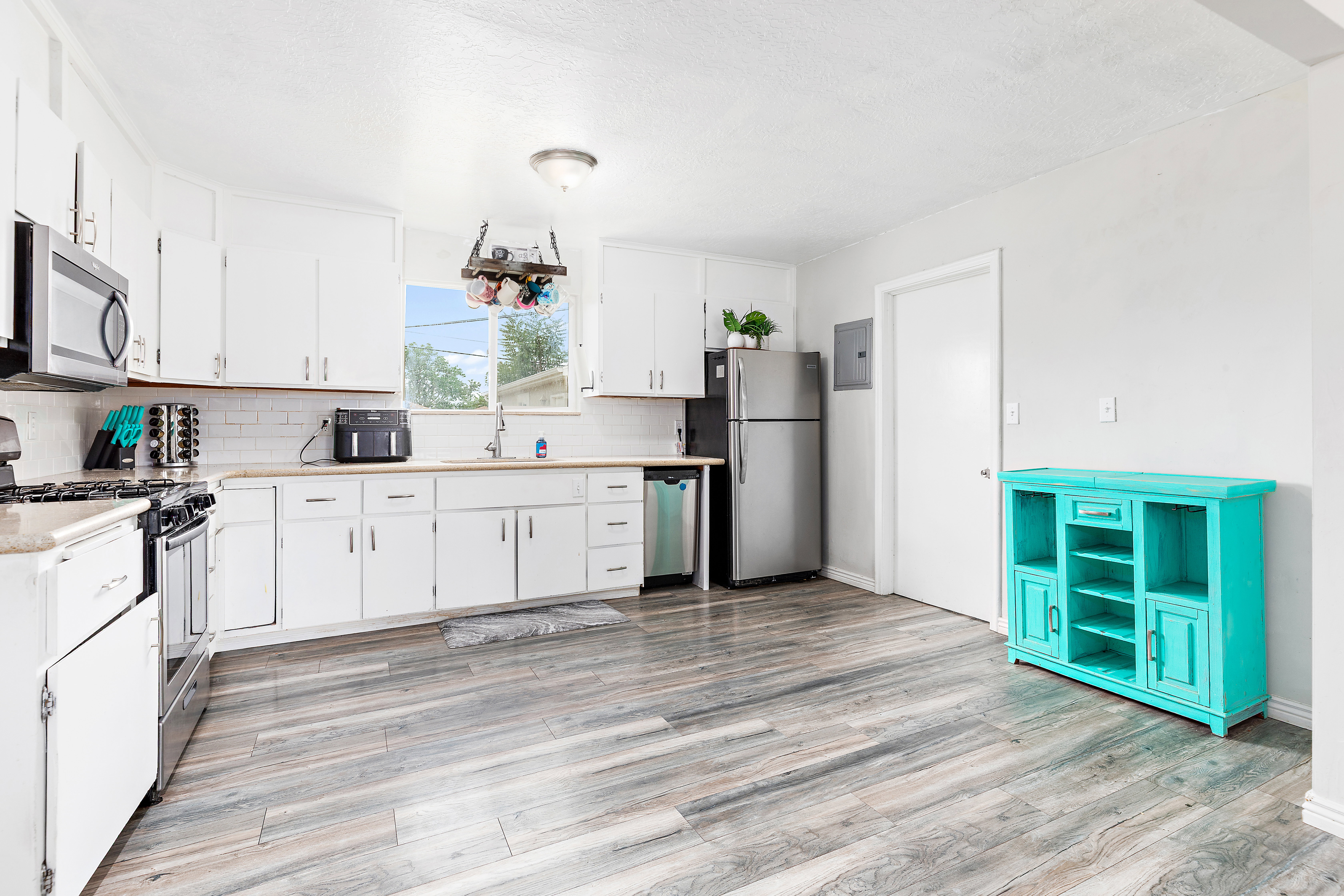 Kitchen featuring white cabinetry, wood-finish flooring, light countertops, subway tile backsplash, and stainless steel appliances