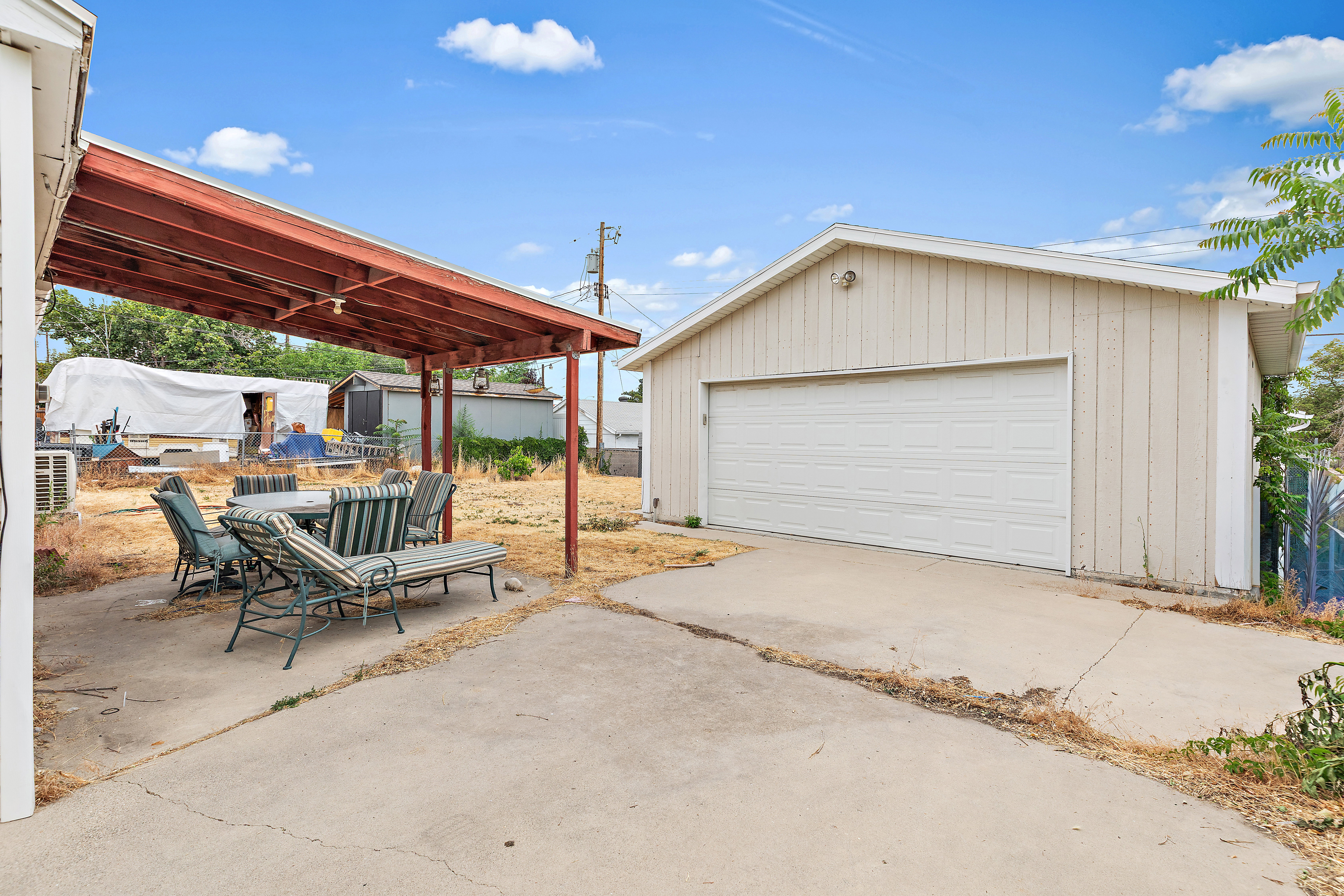Detached garage with a wide garage door, alongside a covered patio area with a concrete slab