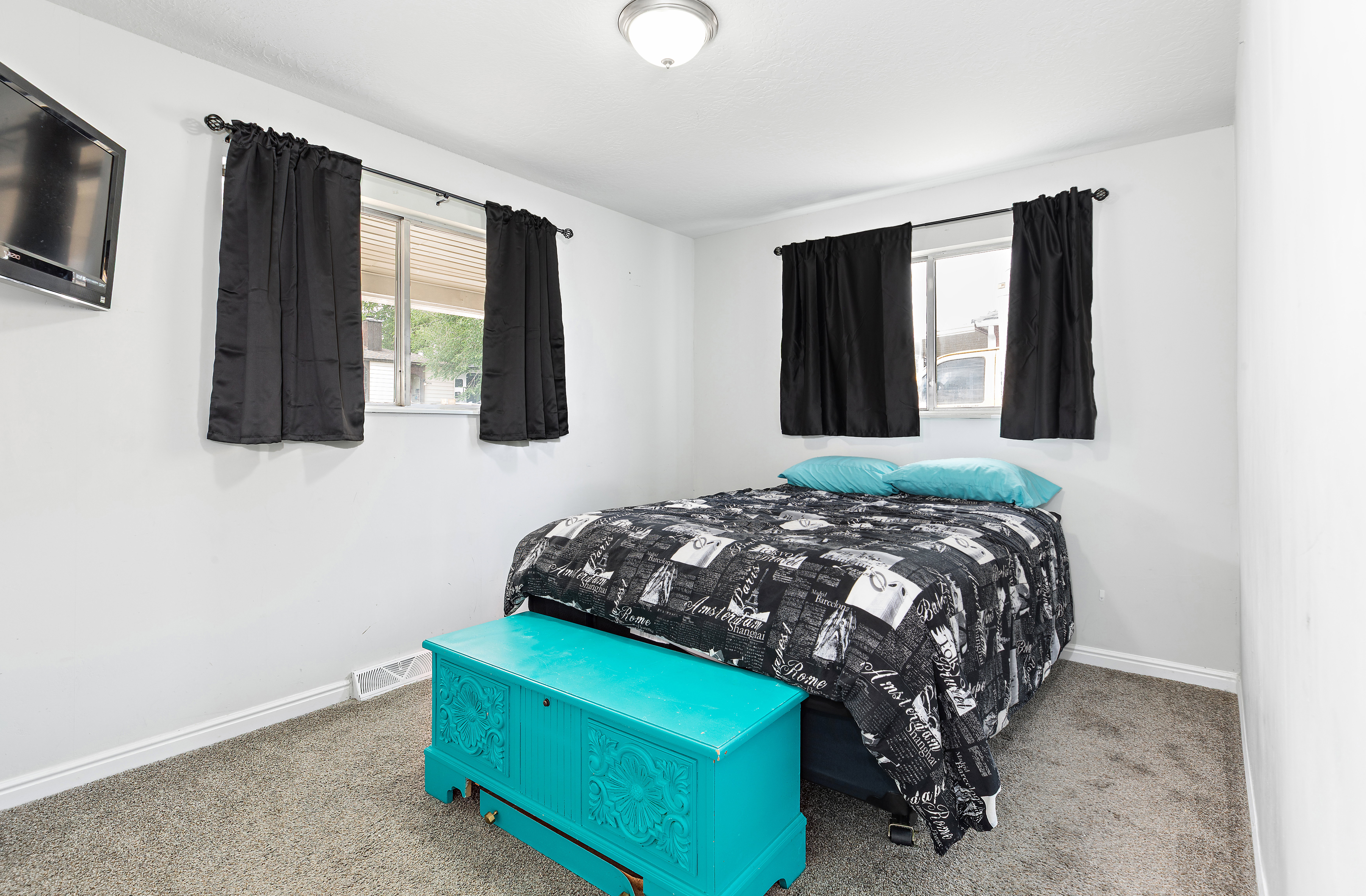 Room featuring two windows with dark curtains, light gray walls, and gray carpet flooring