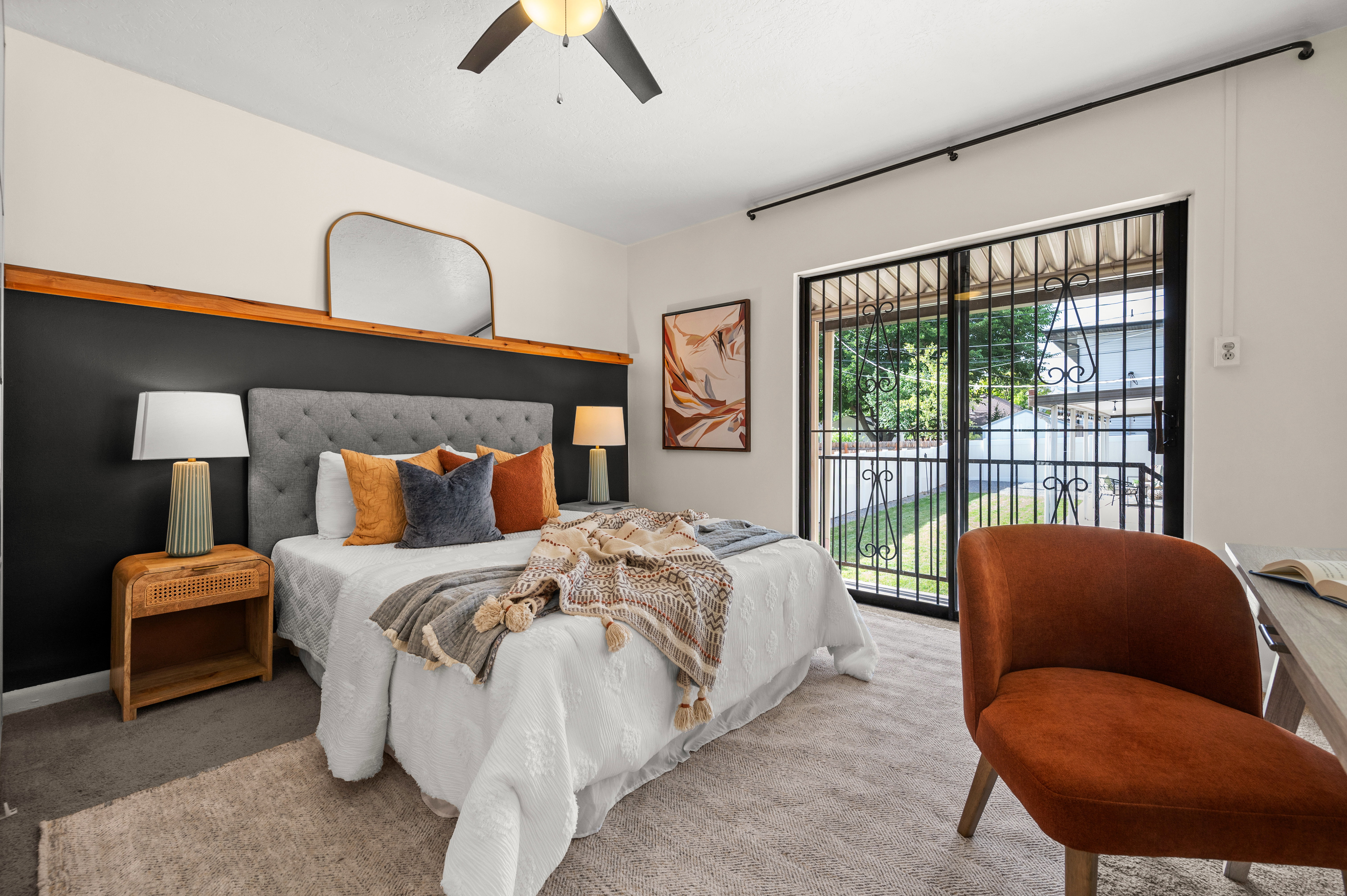 Bedroom featuring a tufted headboard, dark accent wall with wood trim, and a ceiling fan