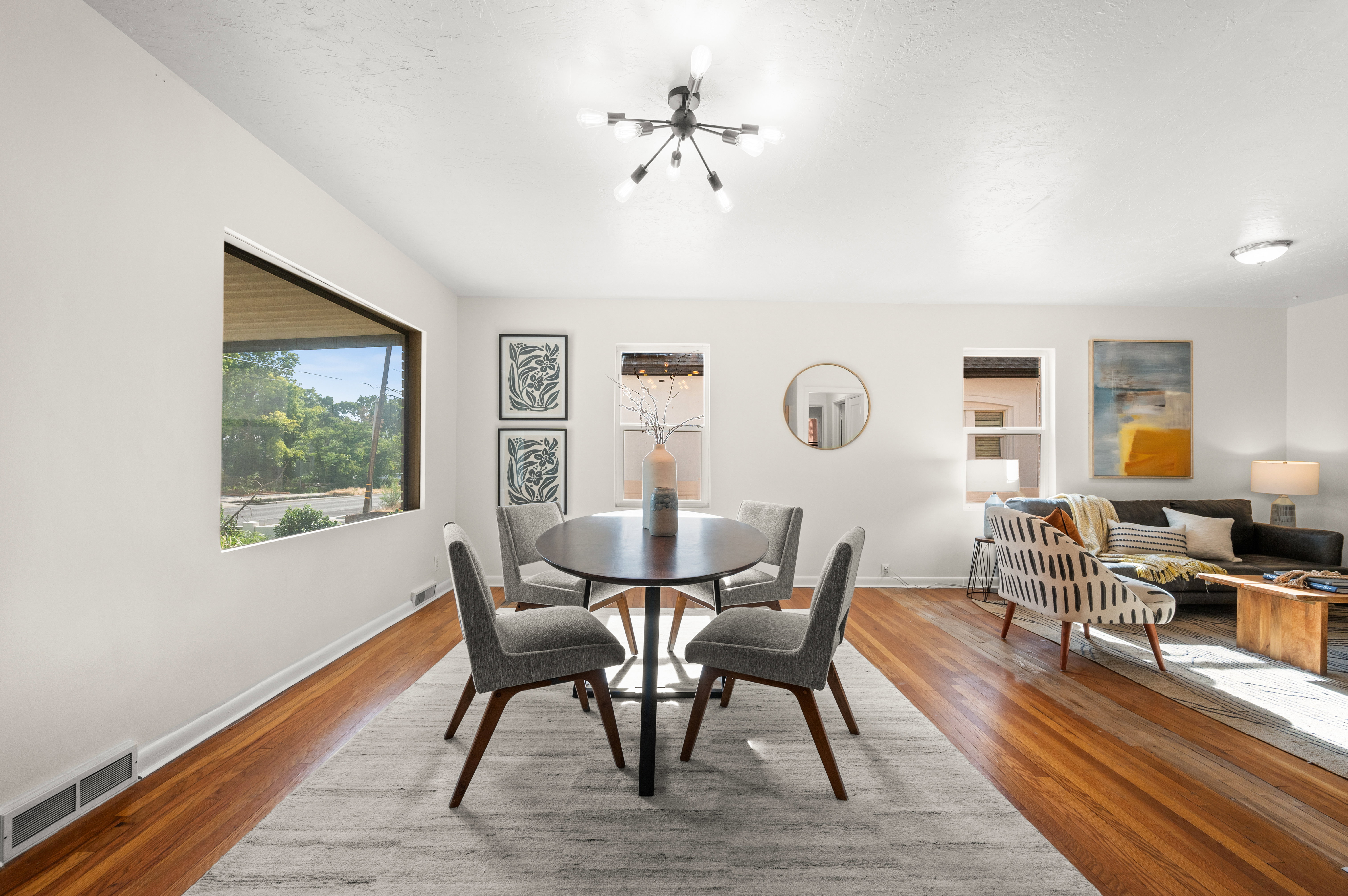 Open-concept living area with polished wood-finish flooring, a contemporary sputnik chandelier, and expansive windows