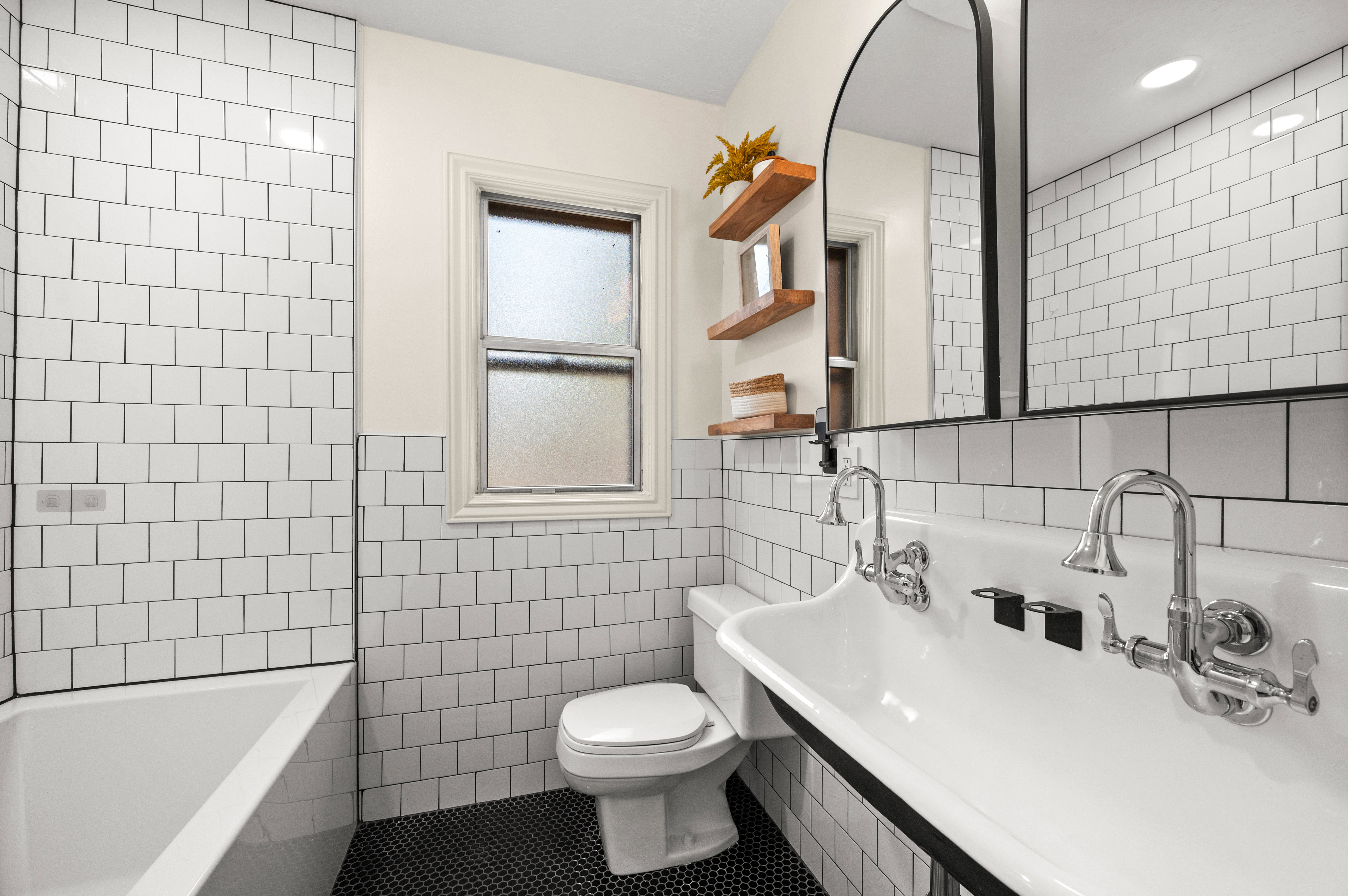 Bathroom featuring a dual basin trough sink with wall-mounted chrome fixtures, white subway tile walls, and dark penny tile flooring