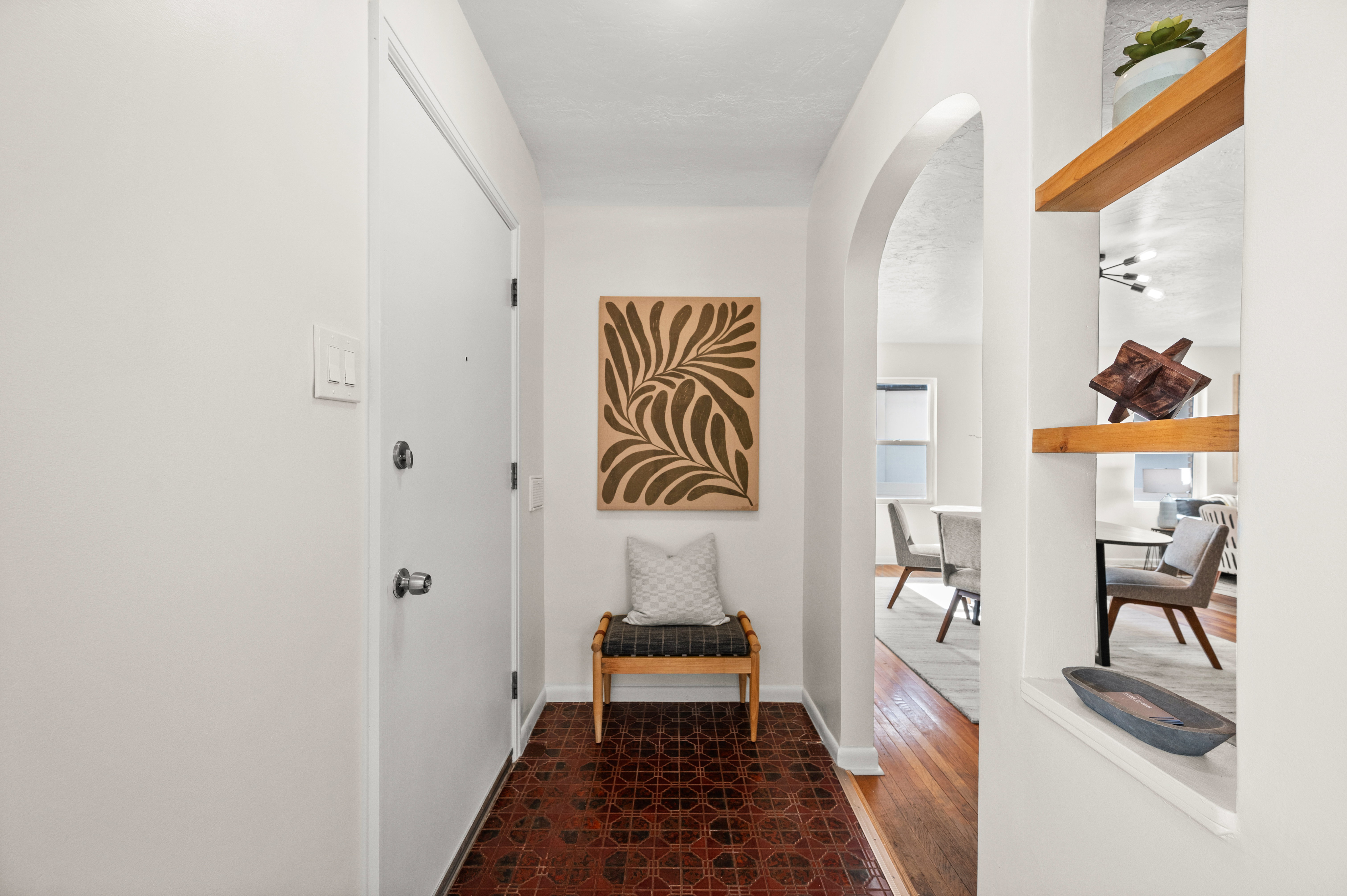 Entryway featuring patterned tile flooring, a white entry door, and an arched doorway leading to interior spaces with wood-finish flooring