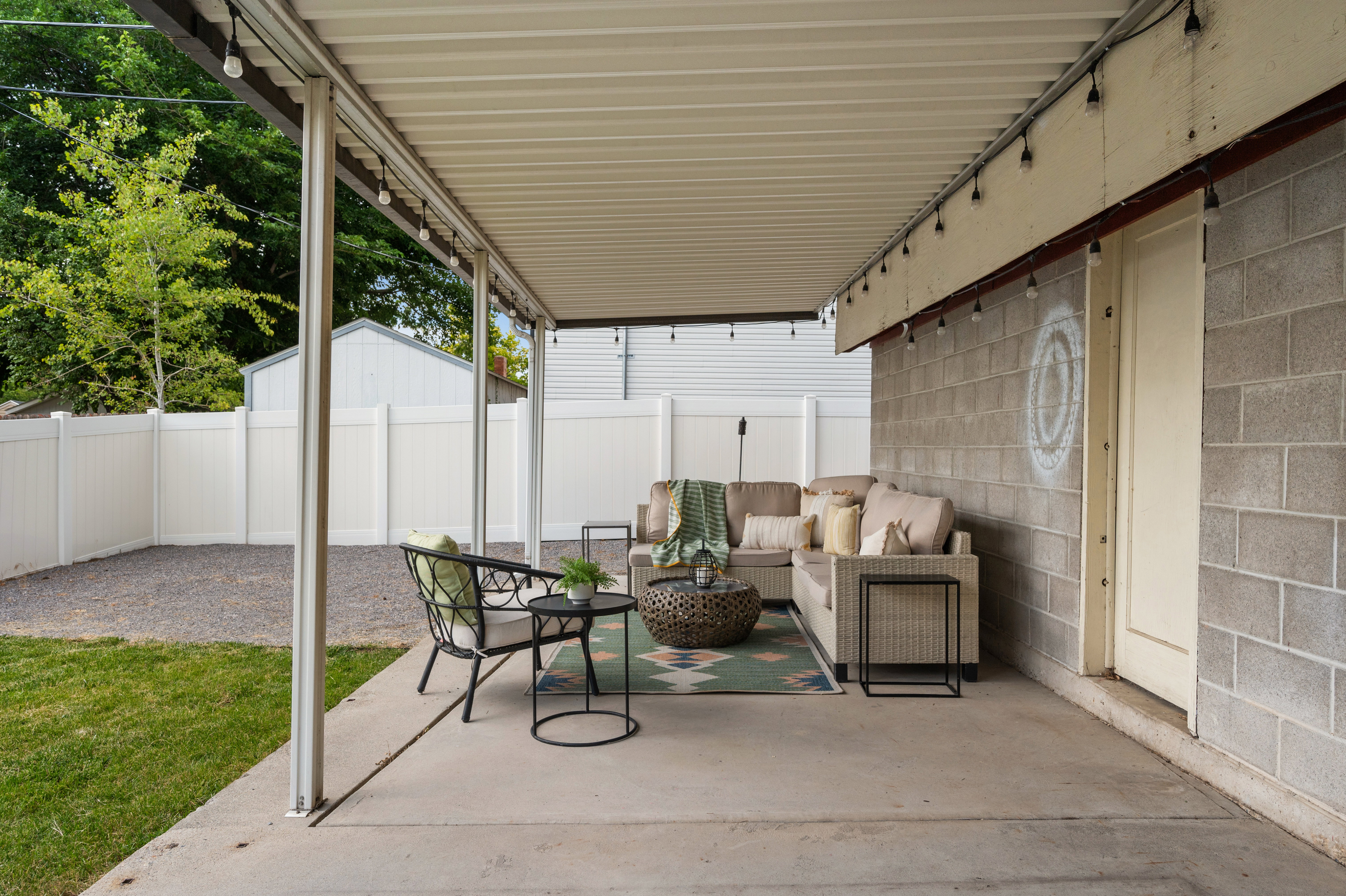 Covered concrete patio featuring string lighting and an exterior block wall