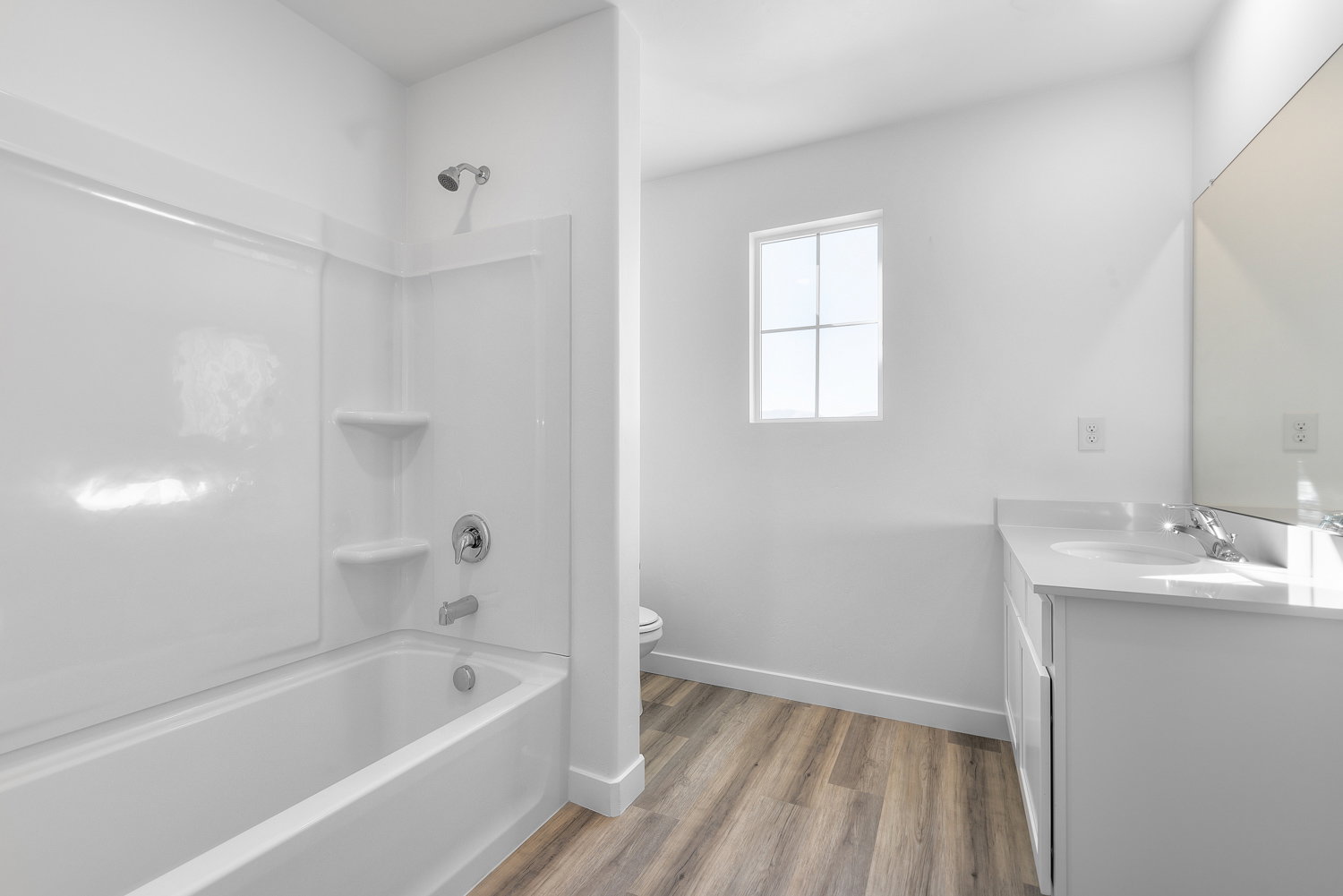 Bathroom featuring a shower-over-tub combination with white surround, a window providing ambient light, wood-finish flooring, a white vanity with a light-colored countertop, and a large wall-mounted mirror