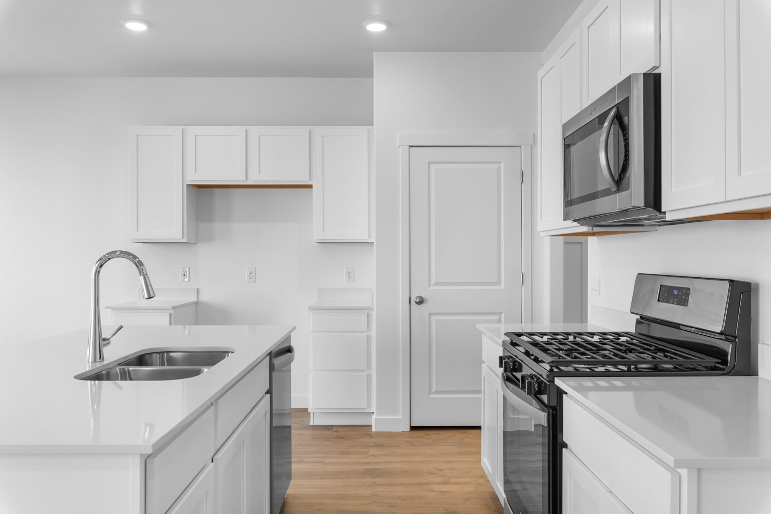 Bright kitchen featuring white shaker cabinetry, stainless steel appliances including a gas range and microwave, light countertops, and wood-finish flooring