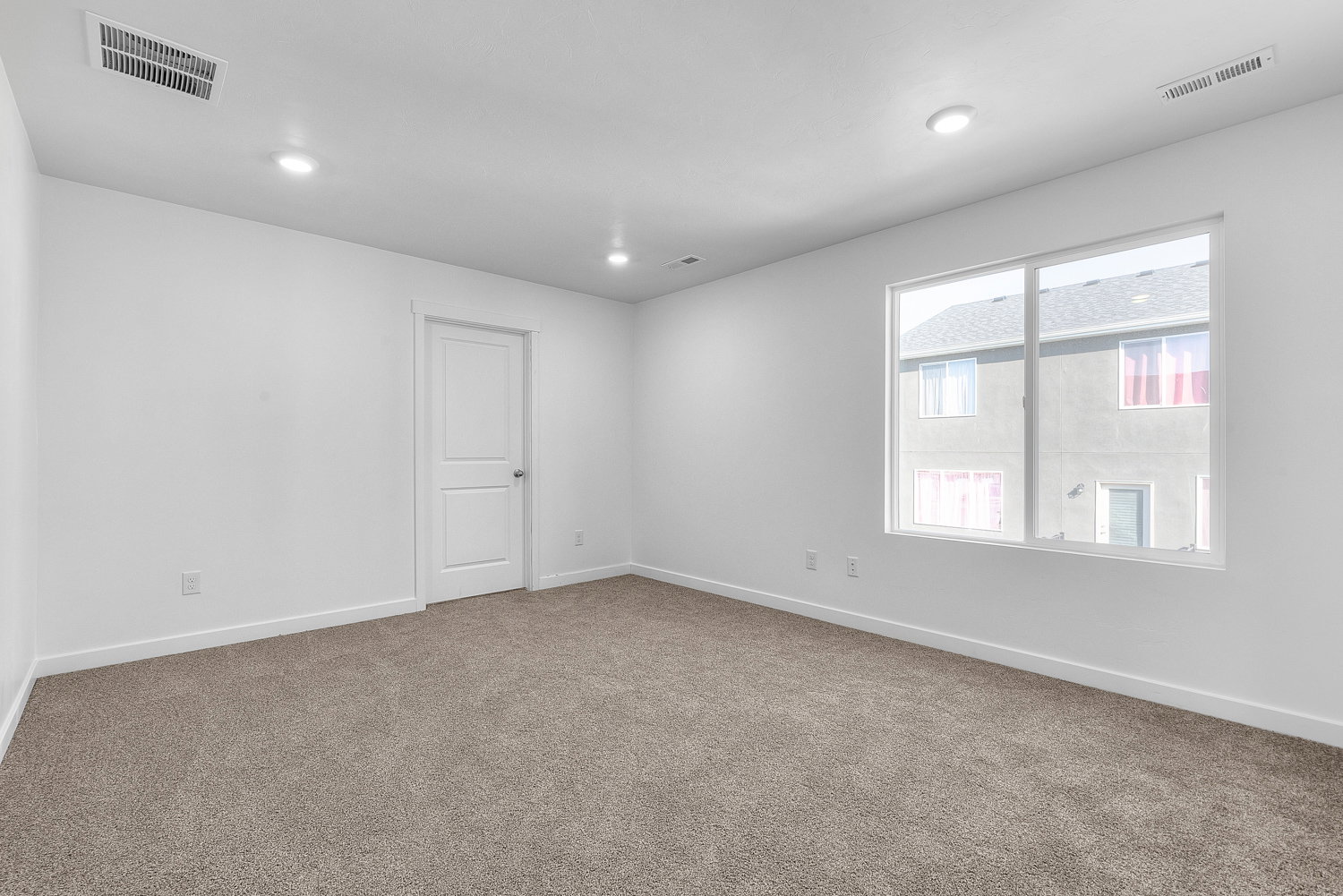 Spacious room featuring neutral carpeting, white walls, recessed lighting, and a large window