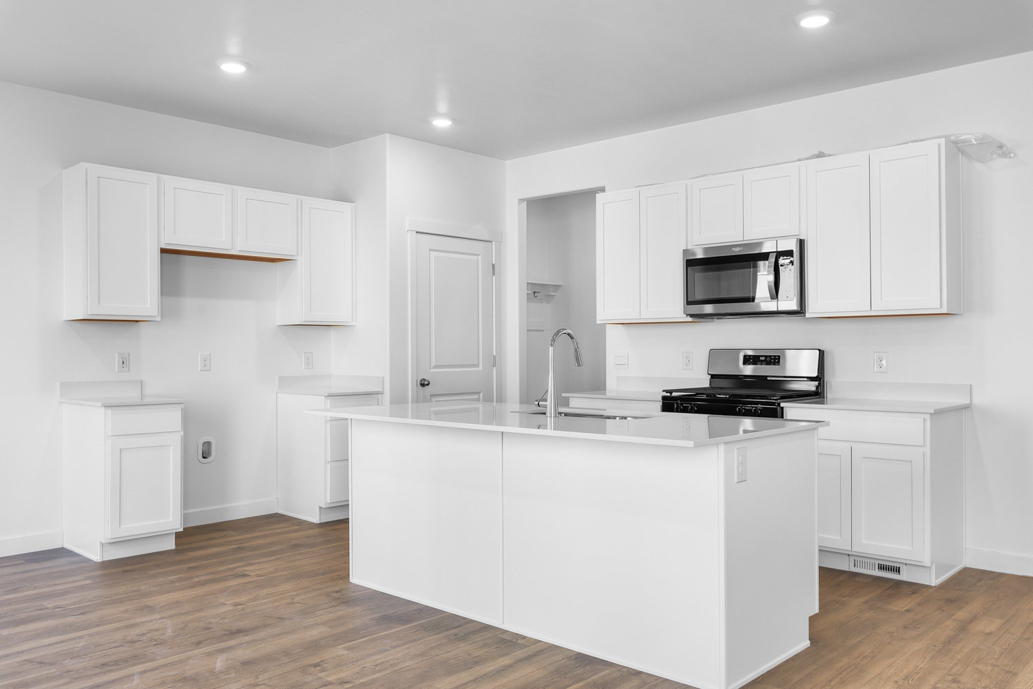Bright kitchen featuring white cabinetry, a central island with an integrated sink, stainless steel appliances, light countertops, and wood-finish flooring