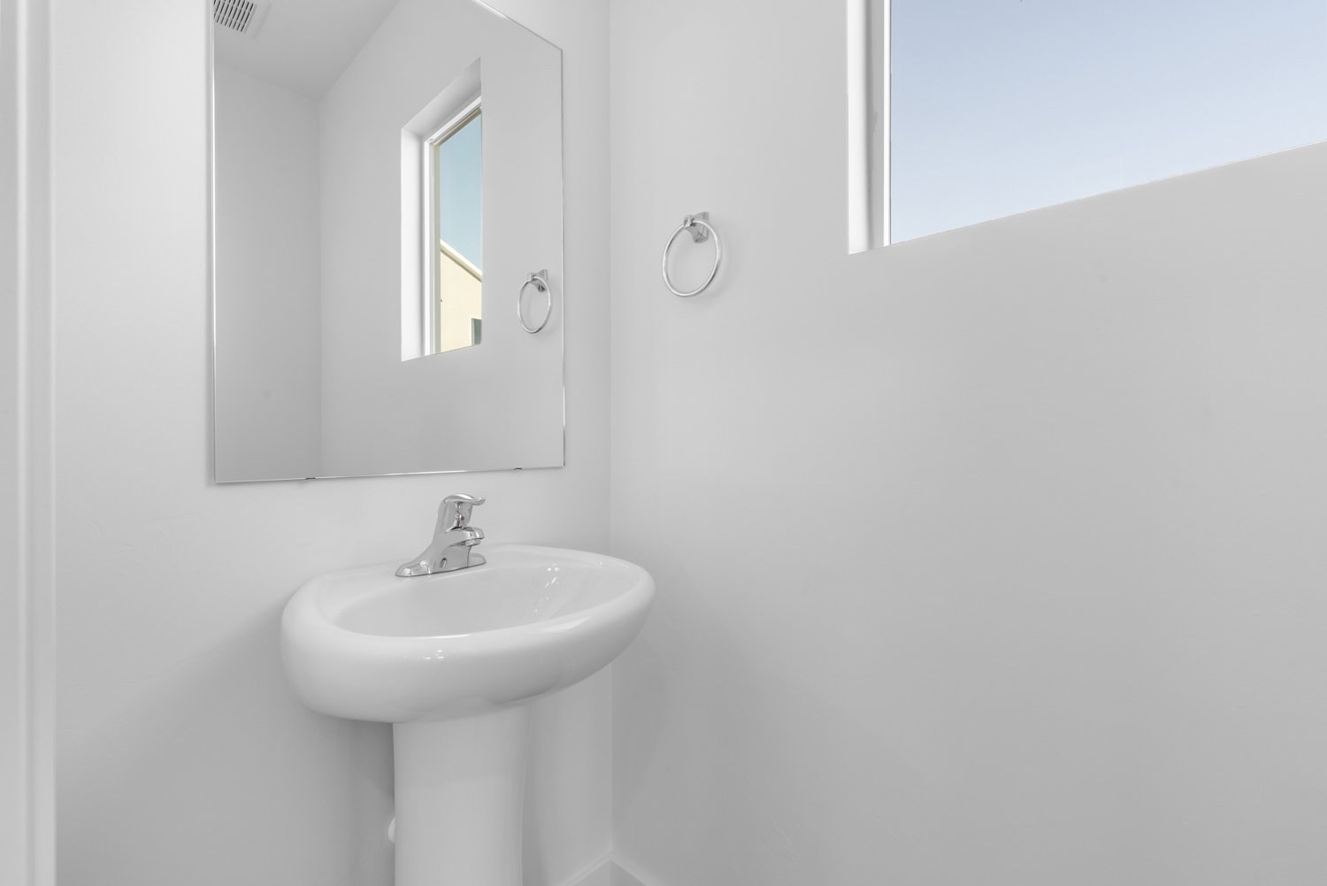 Pedestal sink with chrome faucet, complemented by a rectangular wall mirror