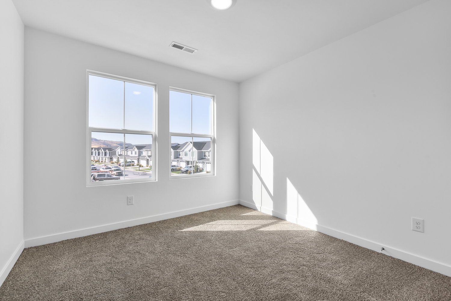 Room featuring two large windows, white walls, and neutral-toned carpet flooring