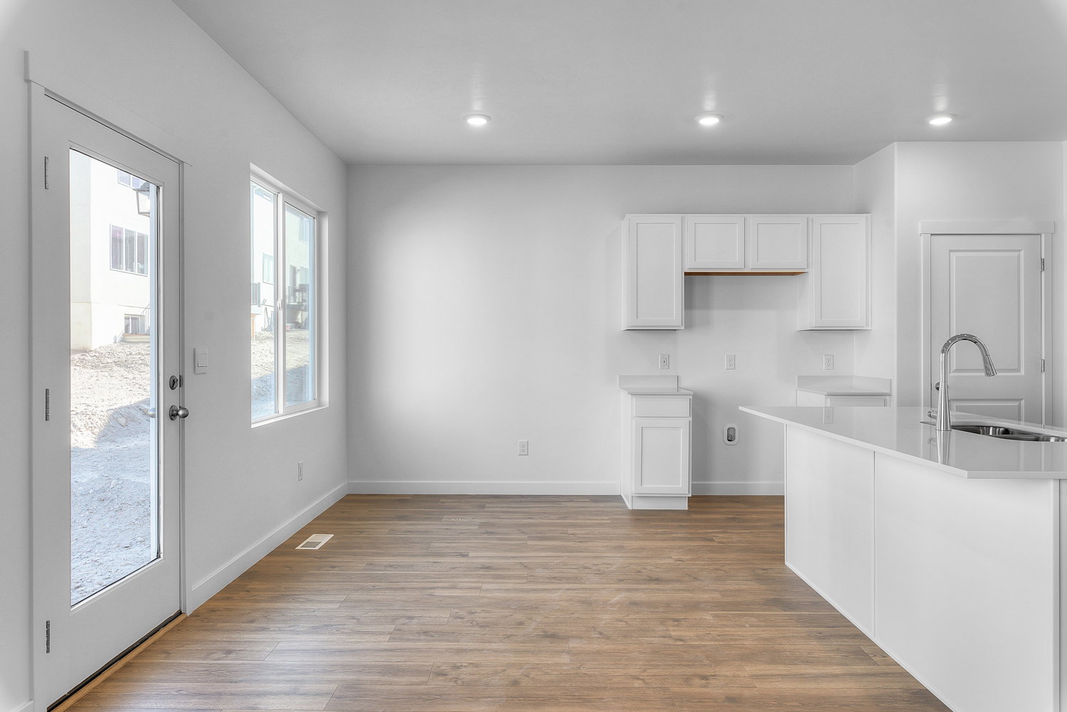 Open-concept kitchen and dining area featuring wood-finish flooring, white cabinetry, a kitchen island with an undermount sink and gooseneck faucet, and recessed lighting