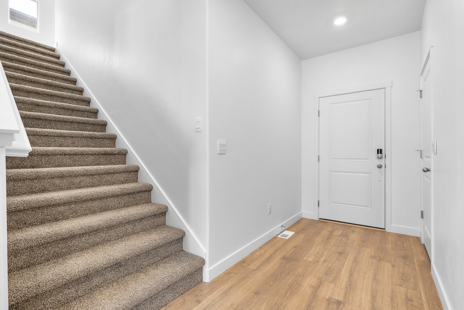Foyer featuring wood-finish flooring, a white paneled entry door with modern hardware, and a carpeted staircase with white trim and railing