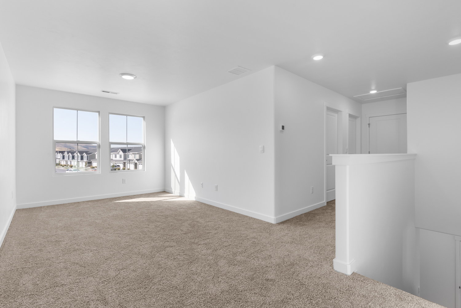 Spacious room with plush carpeting, two large windows, recessed lighting, and crisp white walls