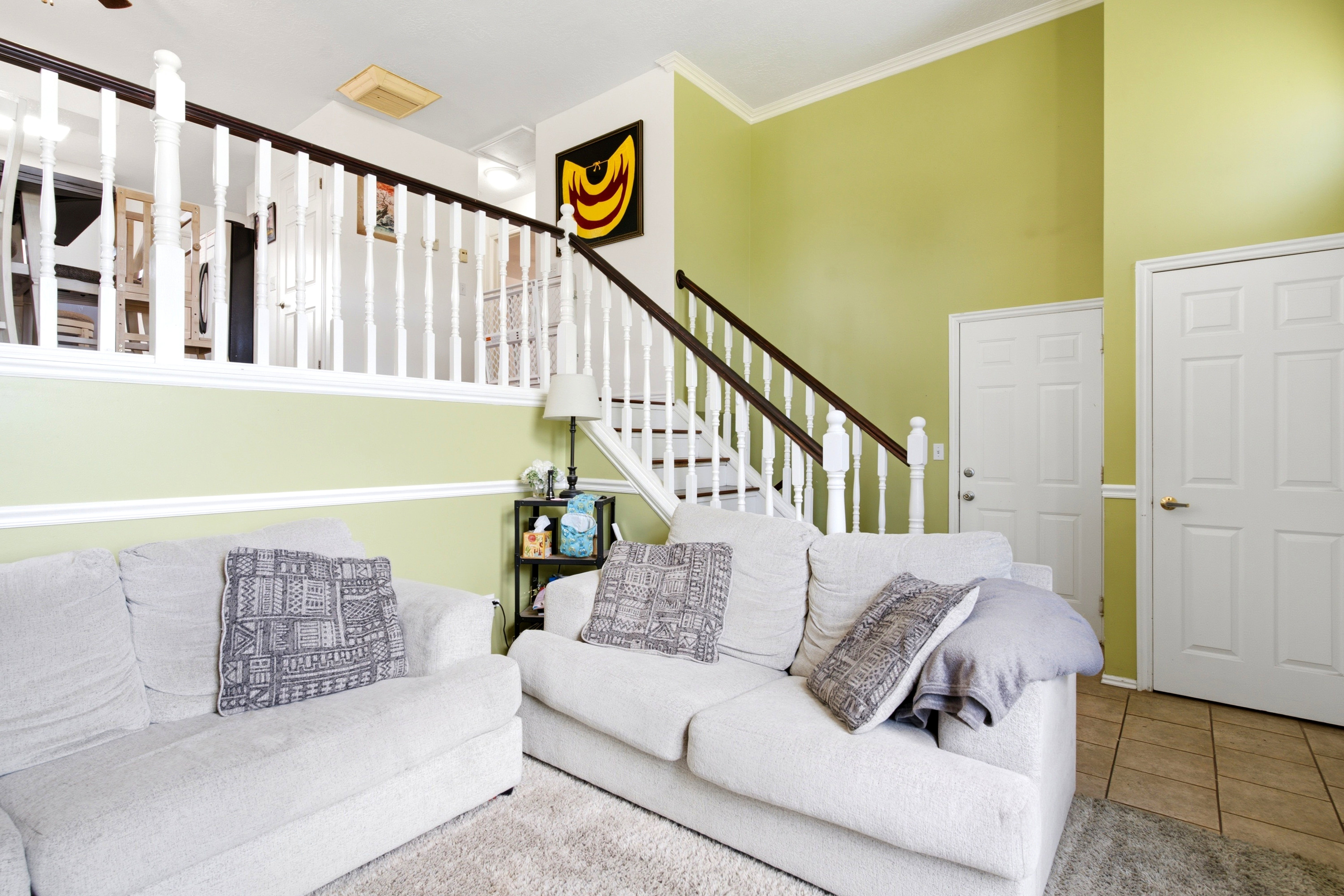 Open-concept living area featuring a two-story ceiling, staircase with white balusters and dark wood handrail, and an upper-level balcony overlooking the space