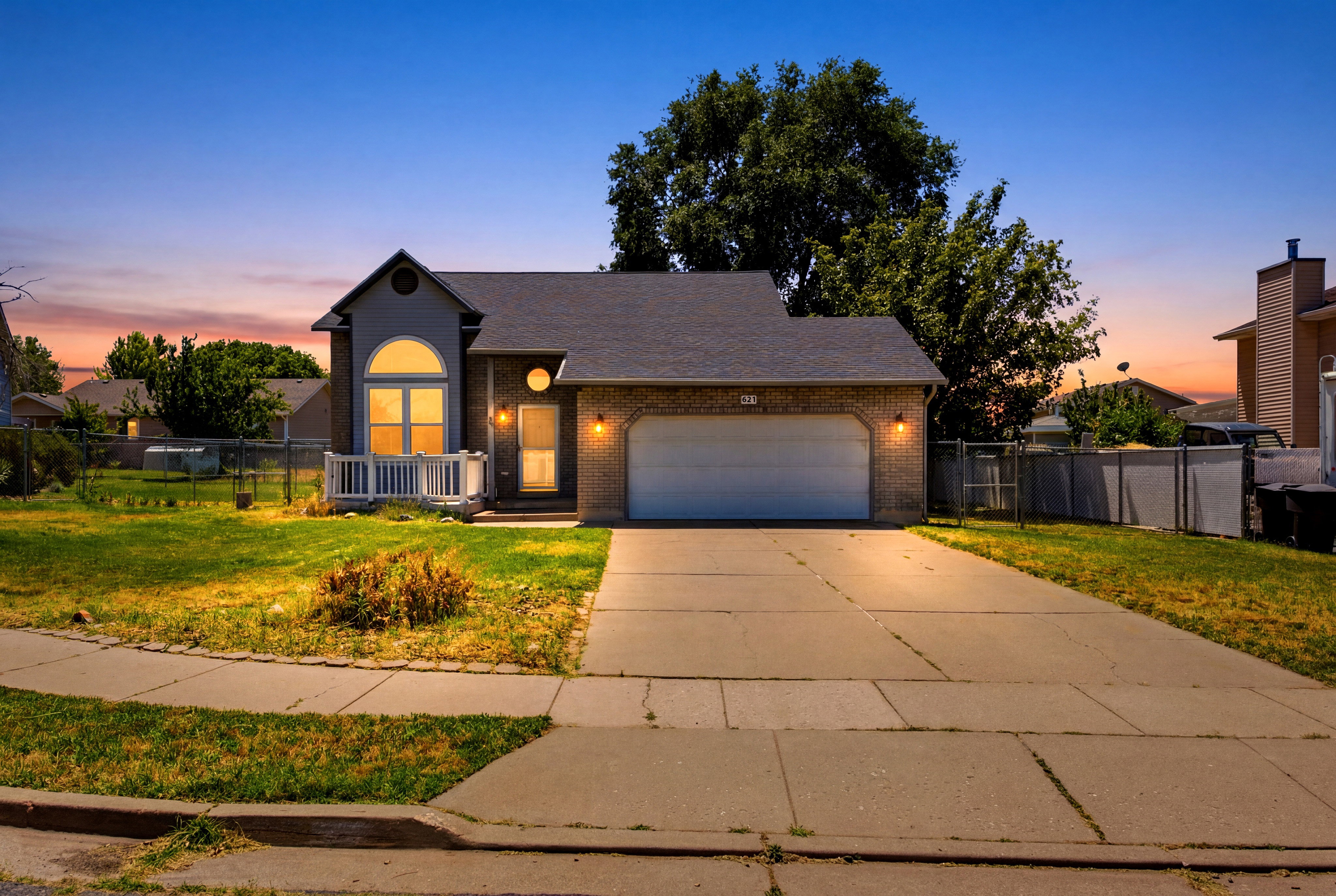 Brick facade residence featuring an arched window, a covered entrance, an attached garage, and a concrete driveway