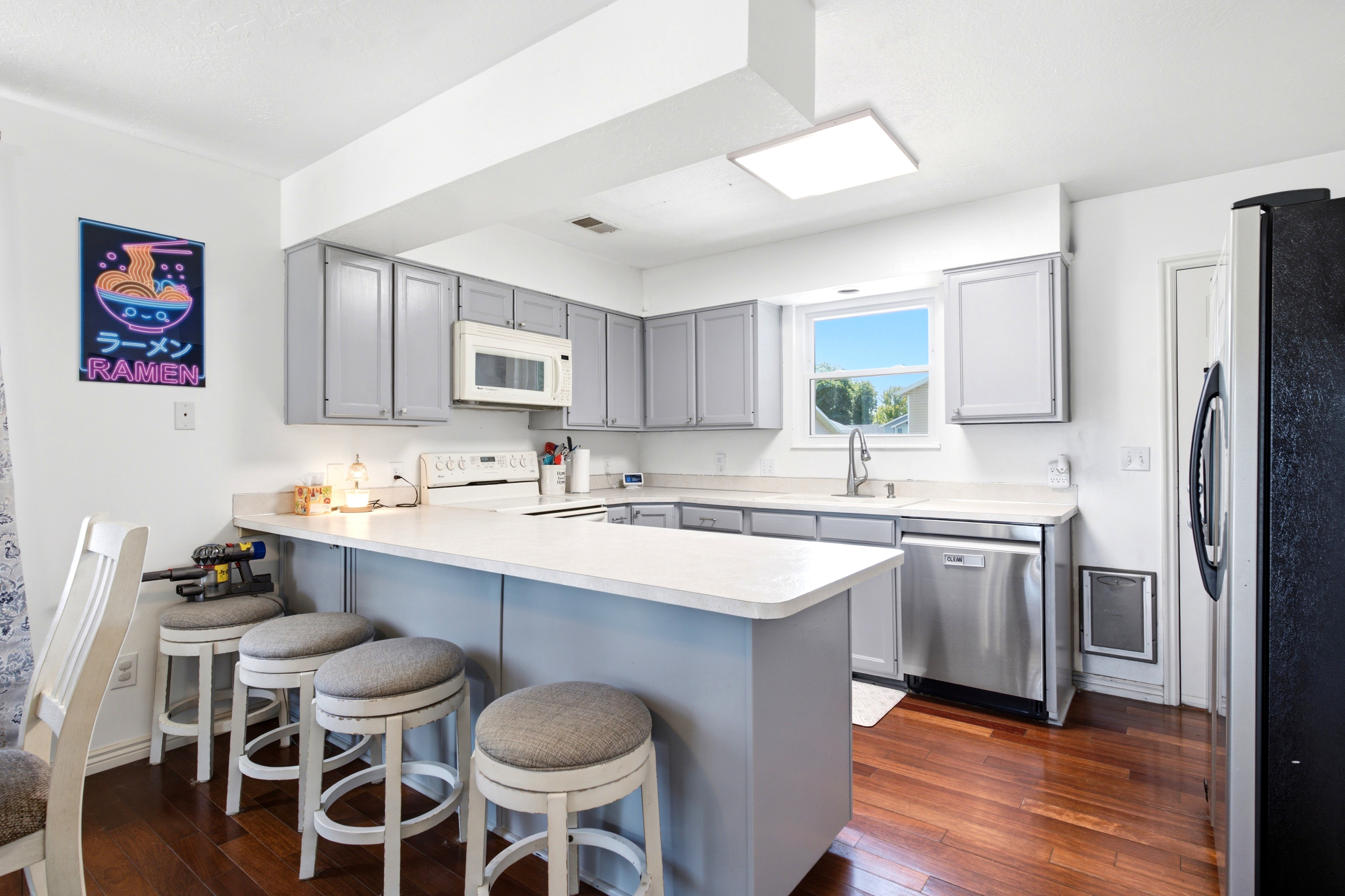 Kitchen featuring a central island with countertop seating, light gray cabinetry, stainless steel dishwasher, white countertop surfaces, and wood-finish flooring