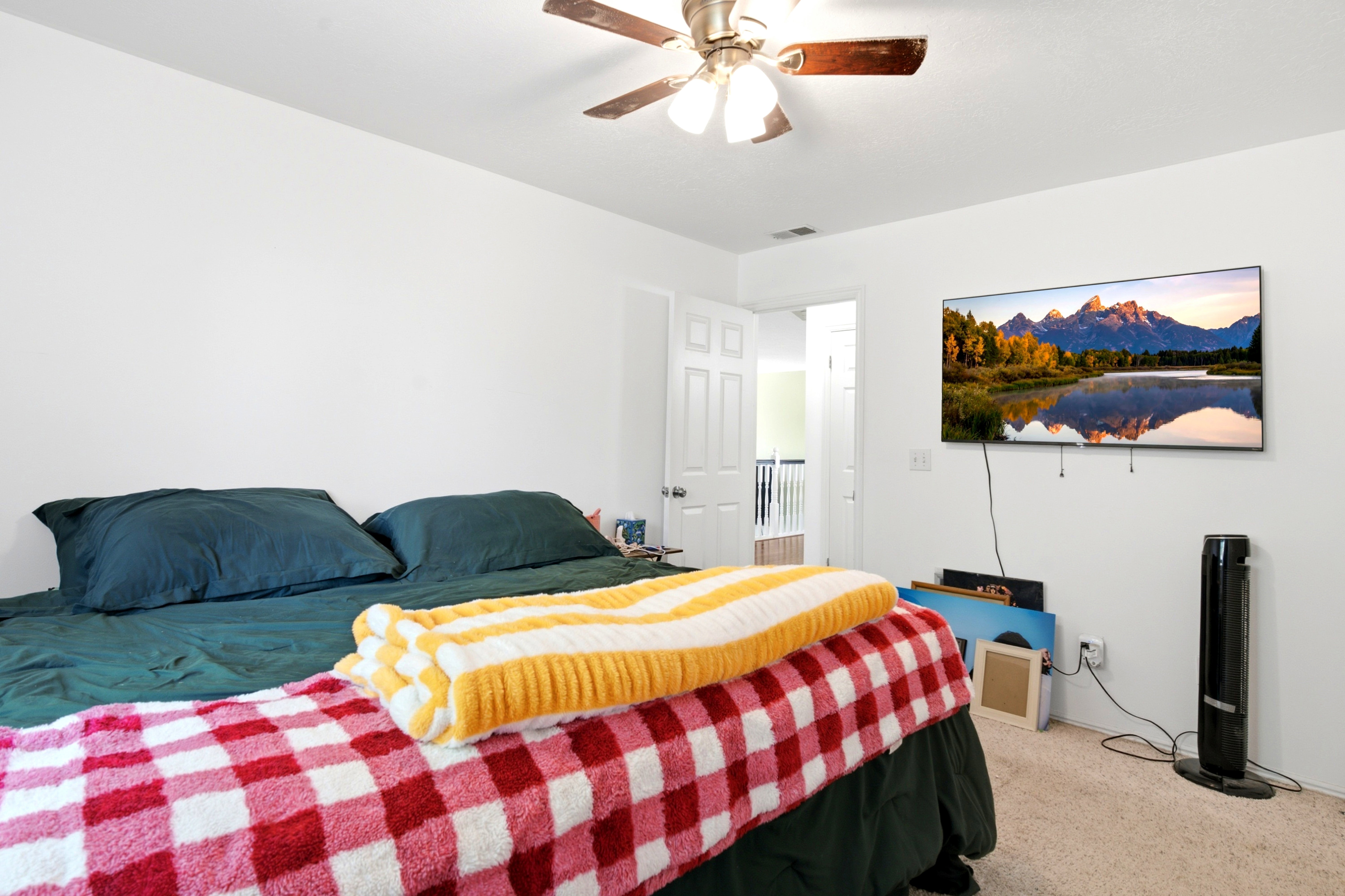 Bedroom featuring neutral wall paint, carpet flooring, a ceiling fan, and a wall-mounted television