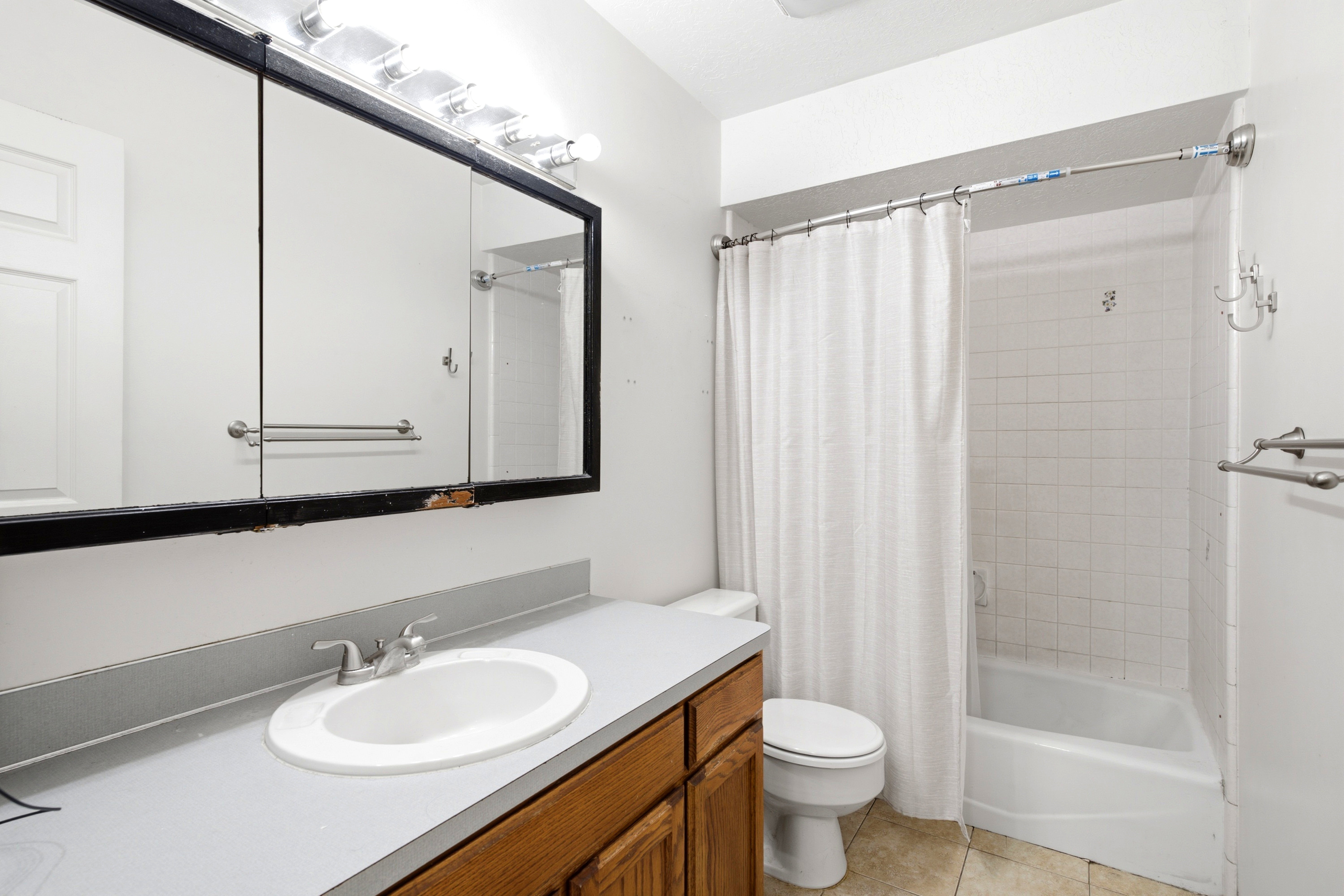 Bathroom featuring a vanity with a laminate countertop and wood-finish cabinetry, a built-in medicine cabinet with integrated lighting, a toilet, a tiled shower and tub combination, and tile flooring